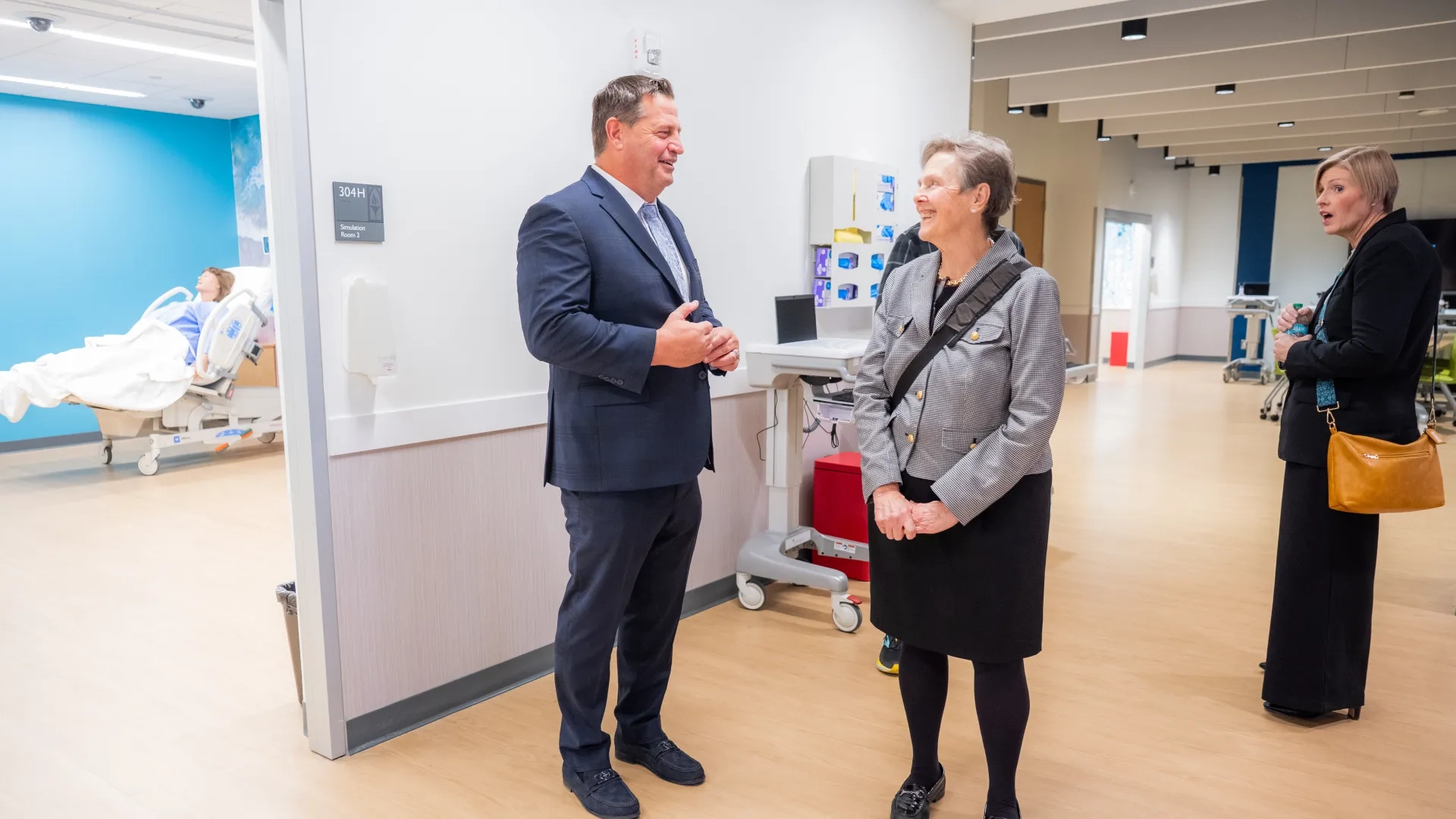 A man and a woman talk outside of a room with a simulated patient