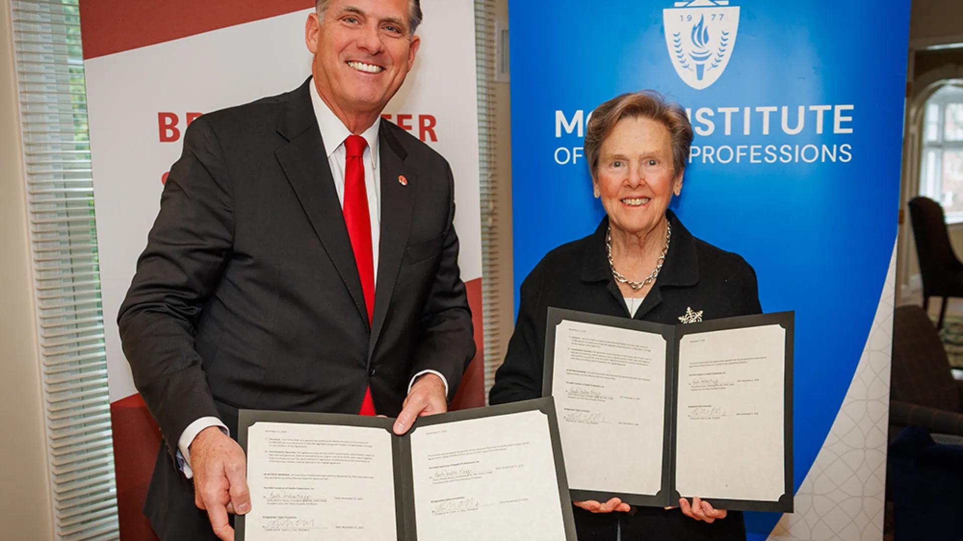Two people standing in front of banners hold documents for others to see