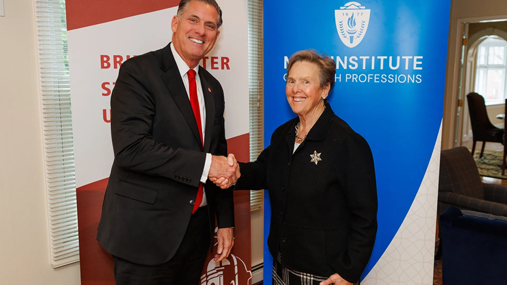 Two people shake hands while standing in front of banners