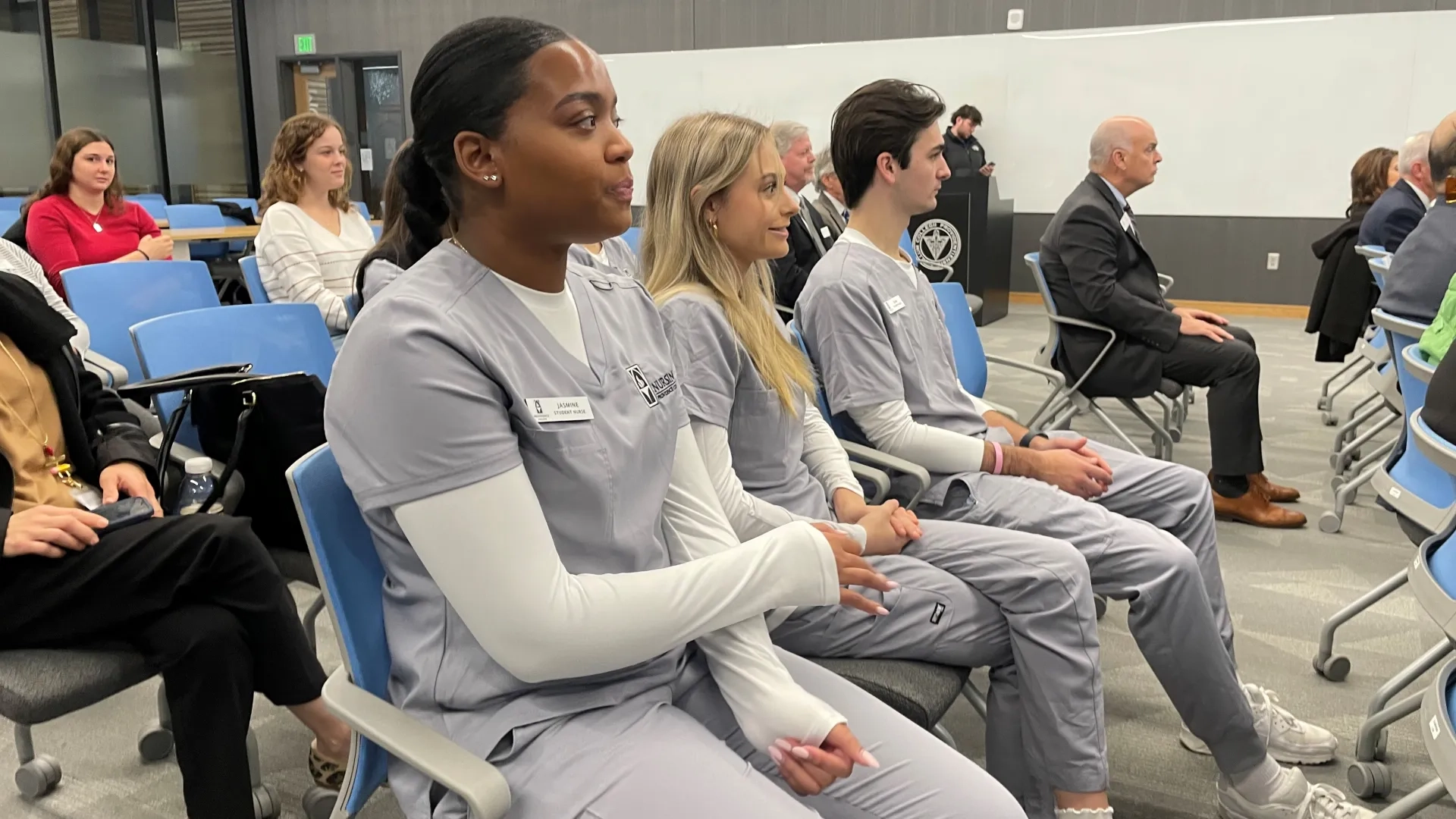 Three people in medical scrubs sit in an audience