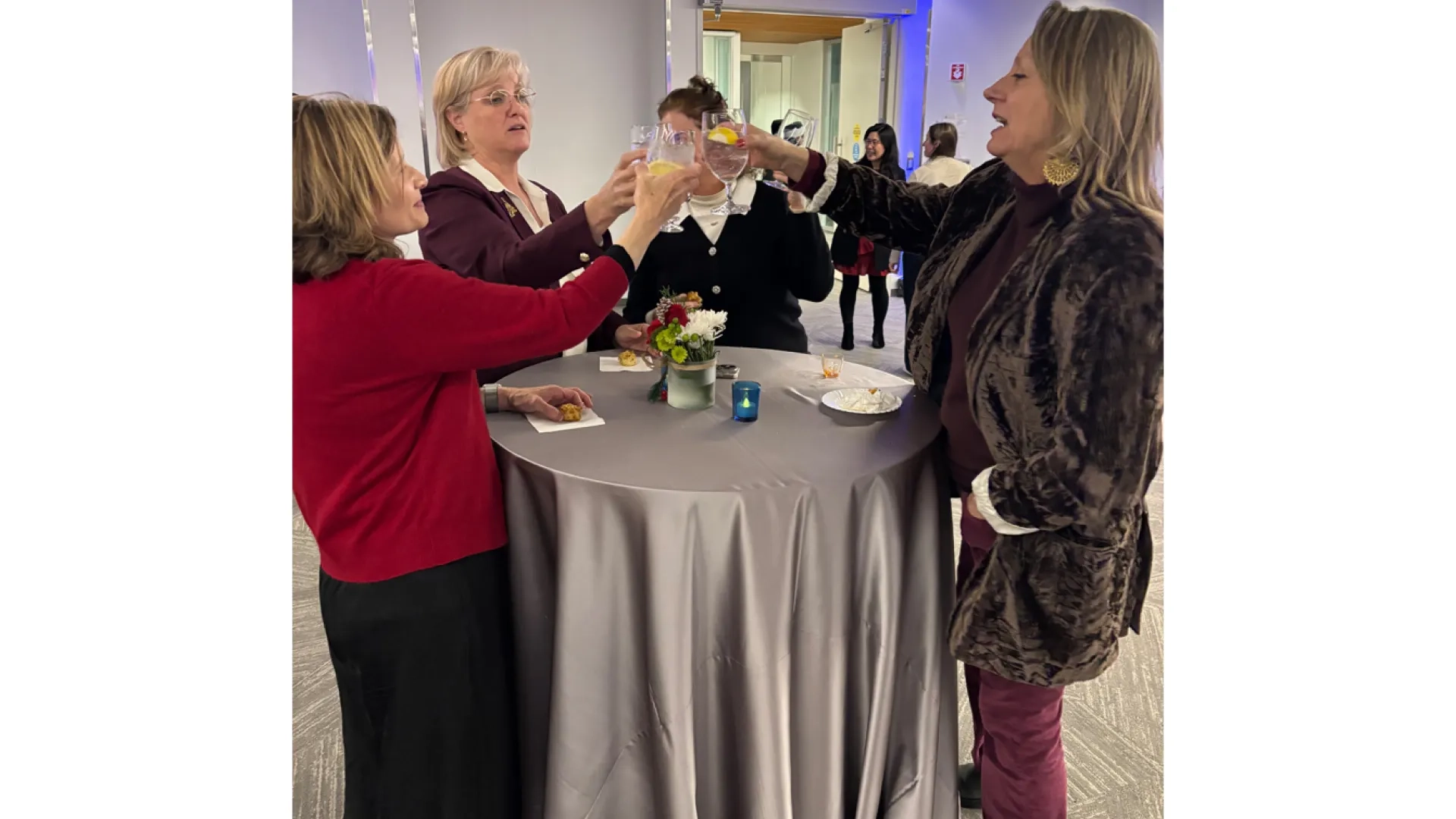 Three women around a table clink glasses