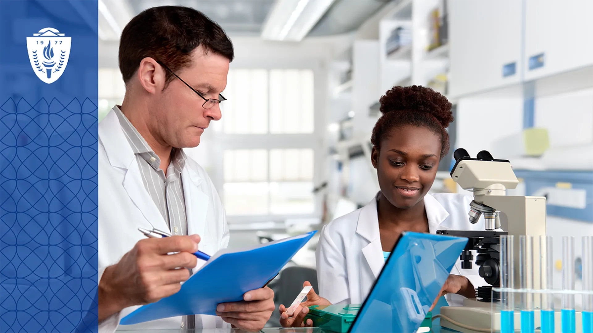 Man and woman wearing lab coats standing in a science lab in front of a microscope and test tubes