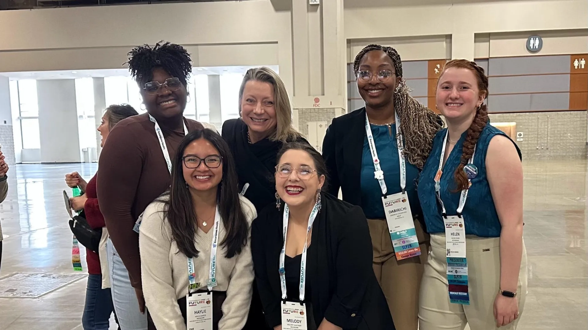 Five women pose in a convention center wearing lanyards