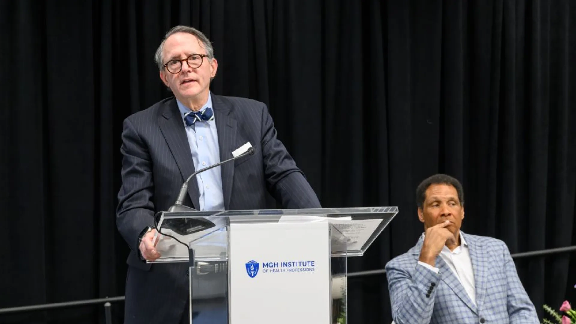 man at a podium and man sitting next to him 