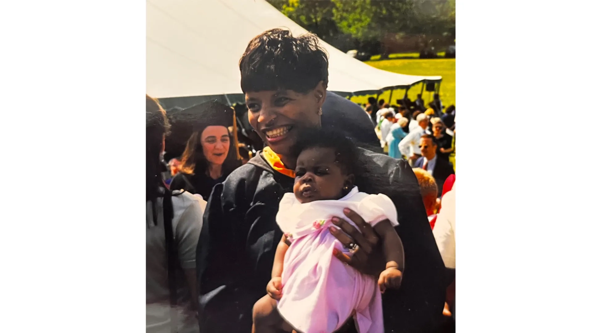 A woman wearing graduation robes holds a baby