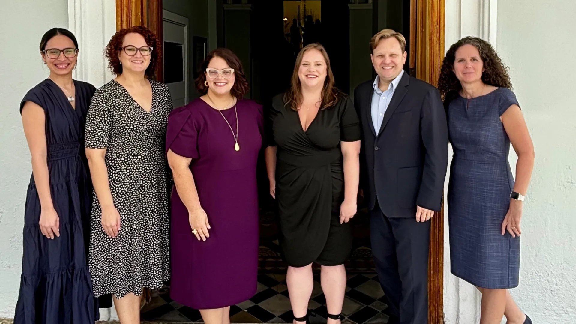 Six people post in front of a doorway