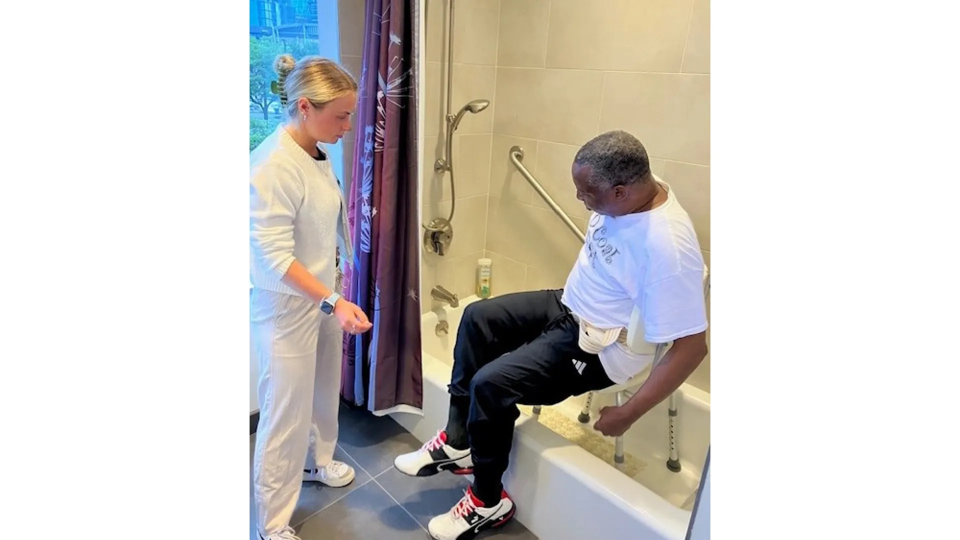 A man uses a chair to help him get into a shower as he practices getting in with help from a woman