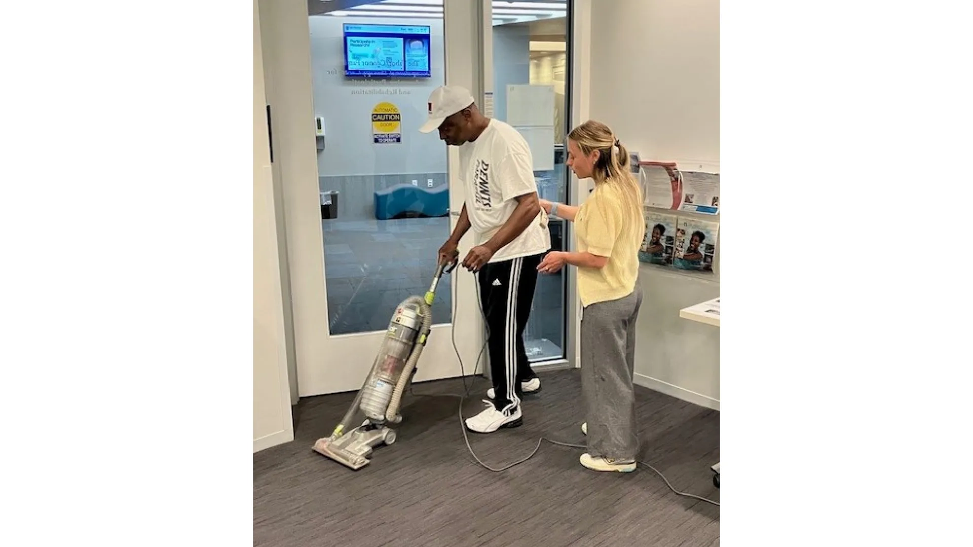 A man vacuums while a woman stands next to him 