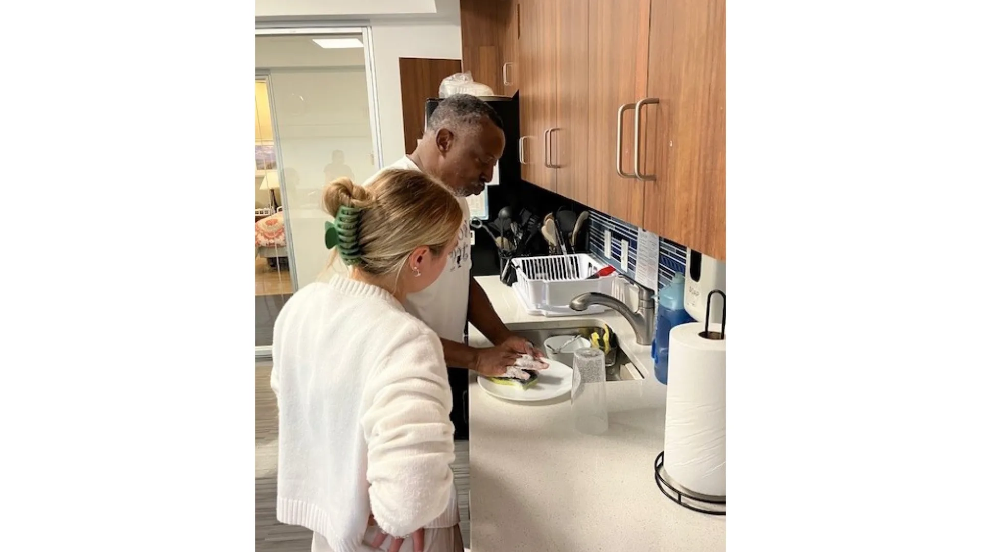 A man cleans a plate in the kitchen while a woman looks on