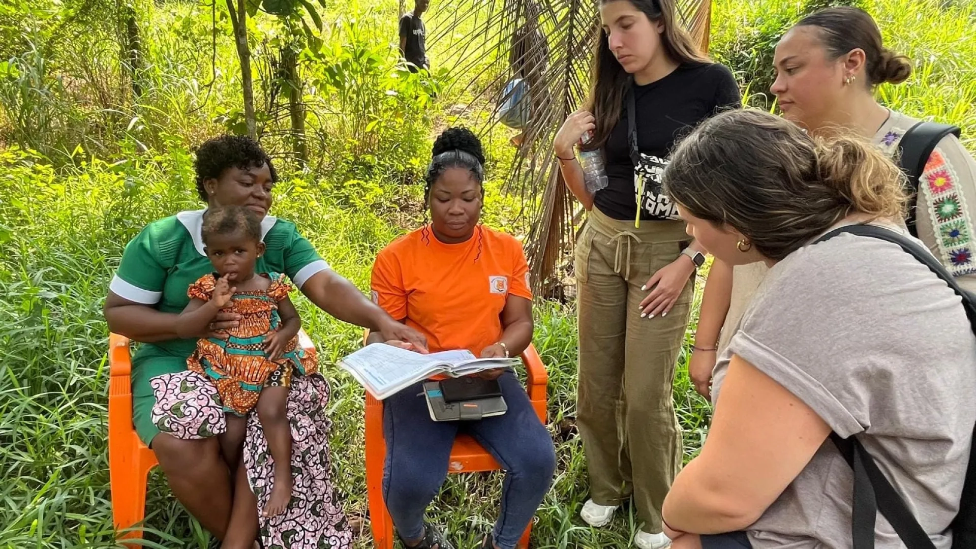 A woman points to a book held by the woman sitting next to her as three women look on