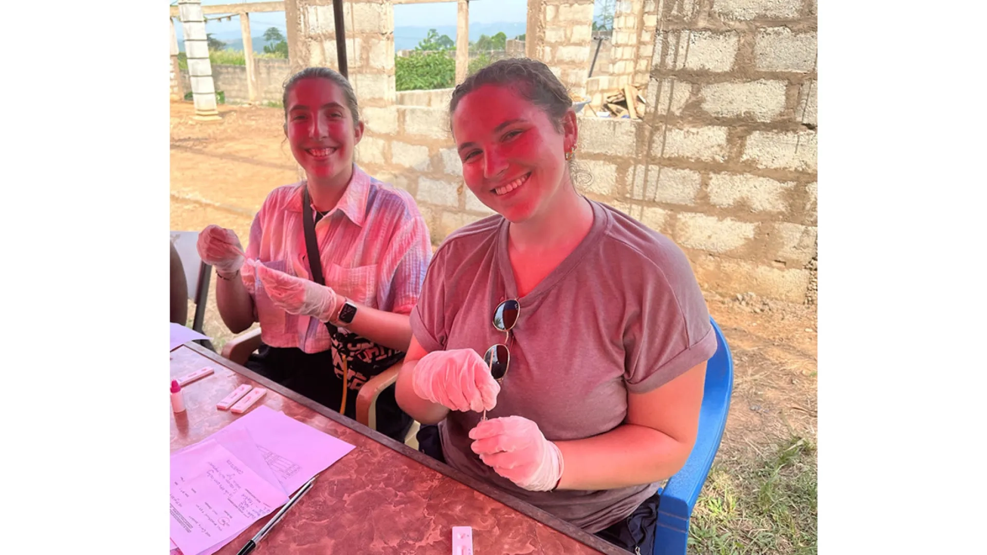 Two women wearing rubber gloves and sitting at a table smile for the camera