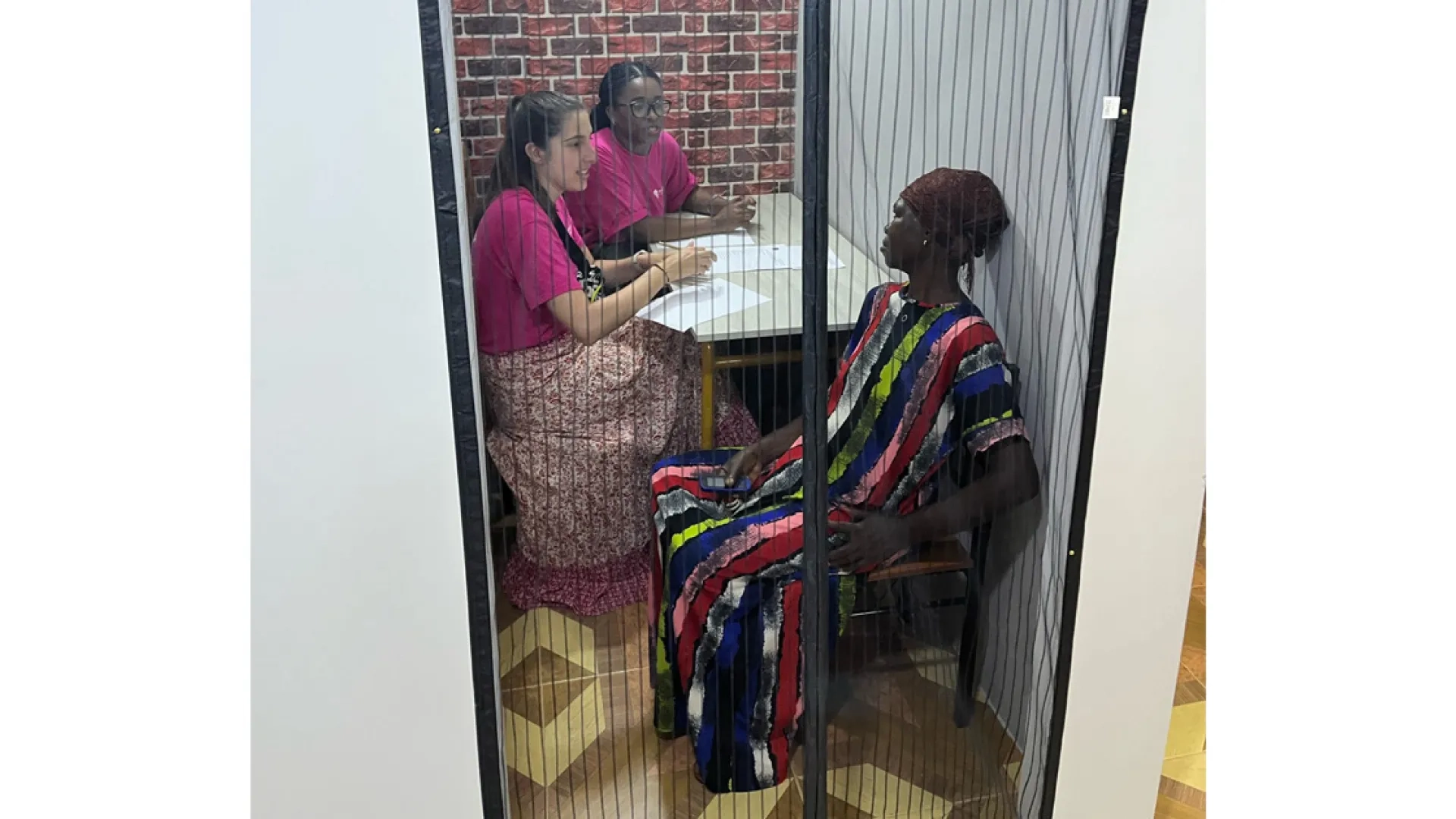 Three women sit at a table in a small room with a screen 