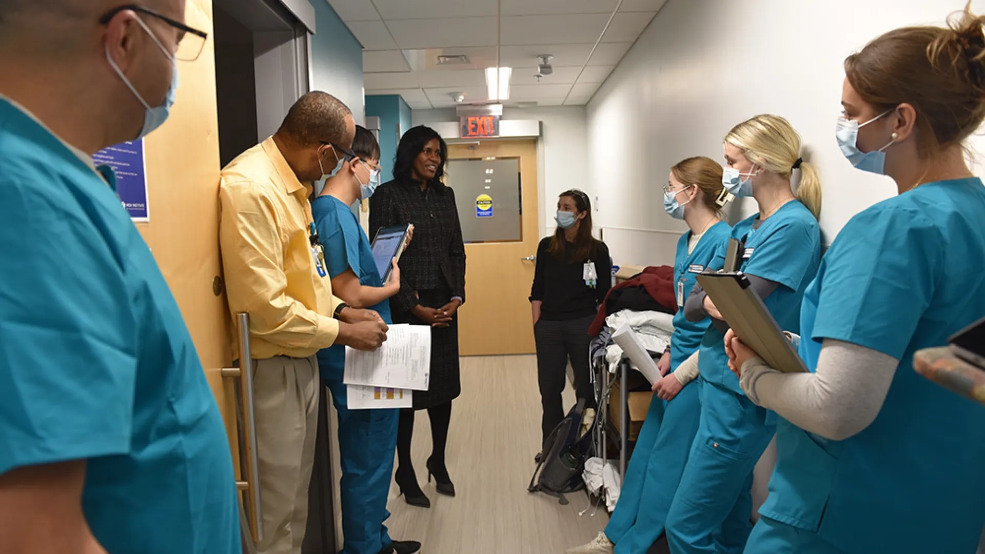 People in medical scrubs stand in a hallway talking to a woman in a suit