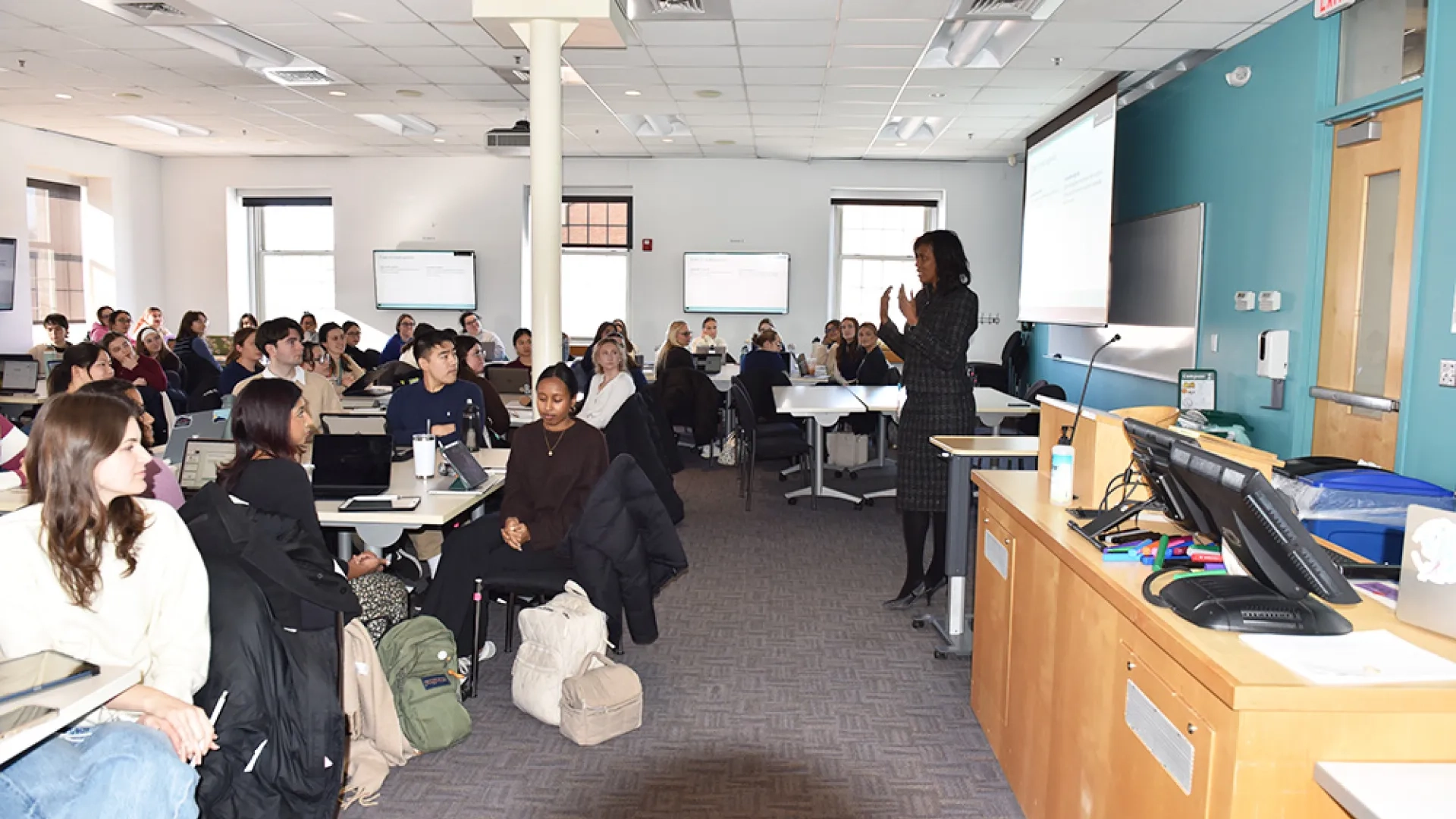 A woman stands in front of a class of students sitting at tables