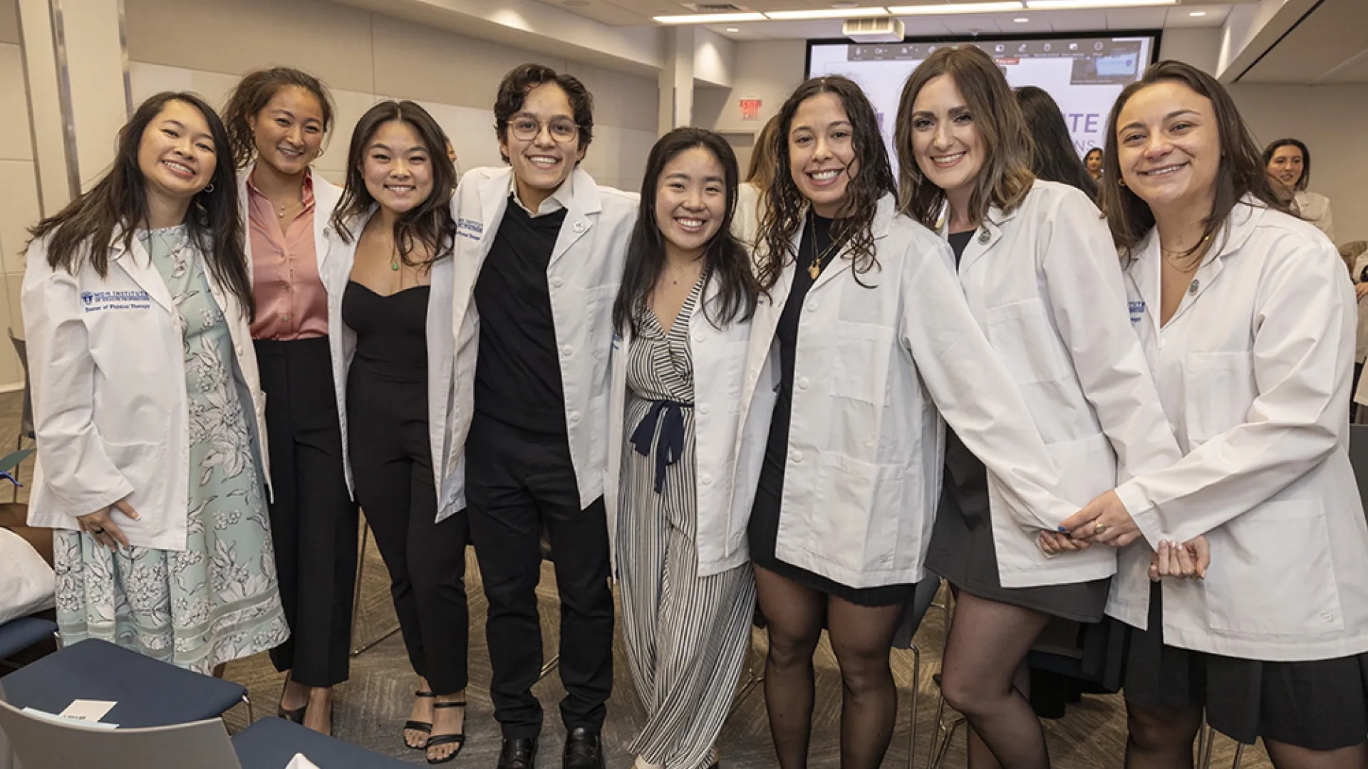 Eight people wearing white coats pose for a photo. 