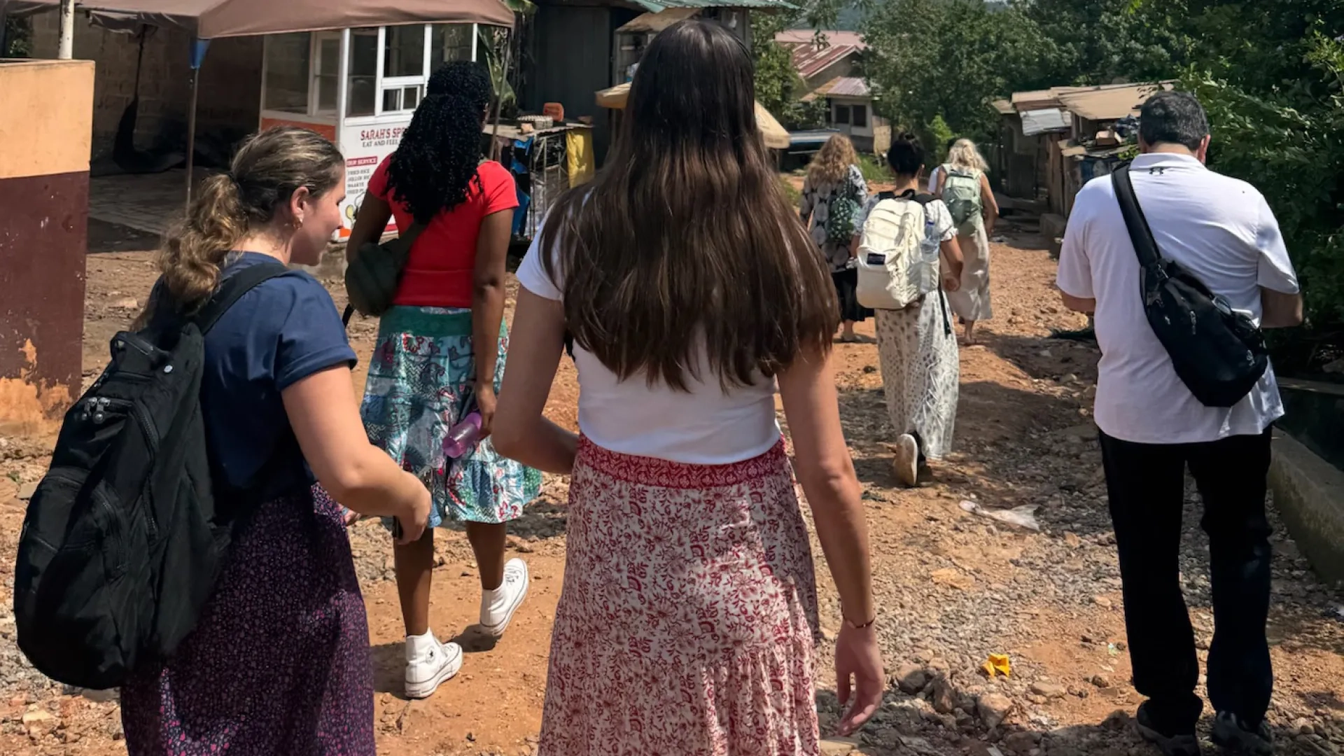 A group of people walking away from the camera on a dirt road