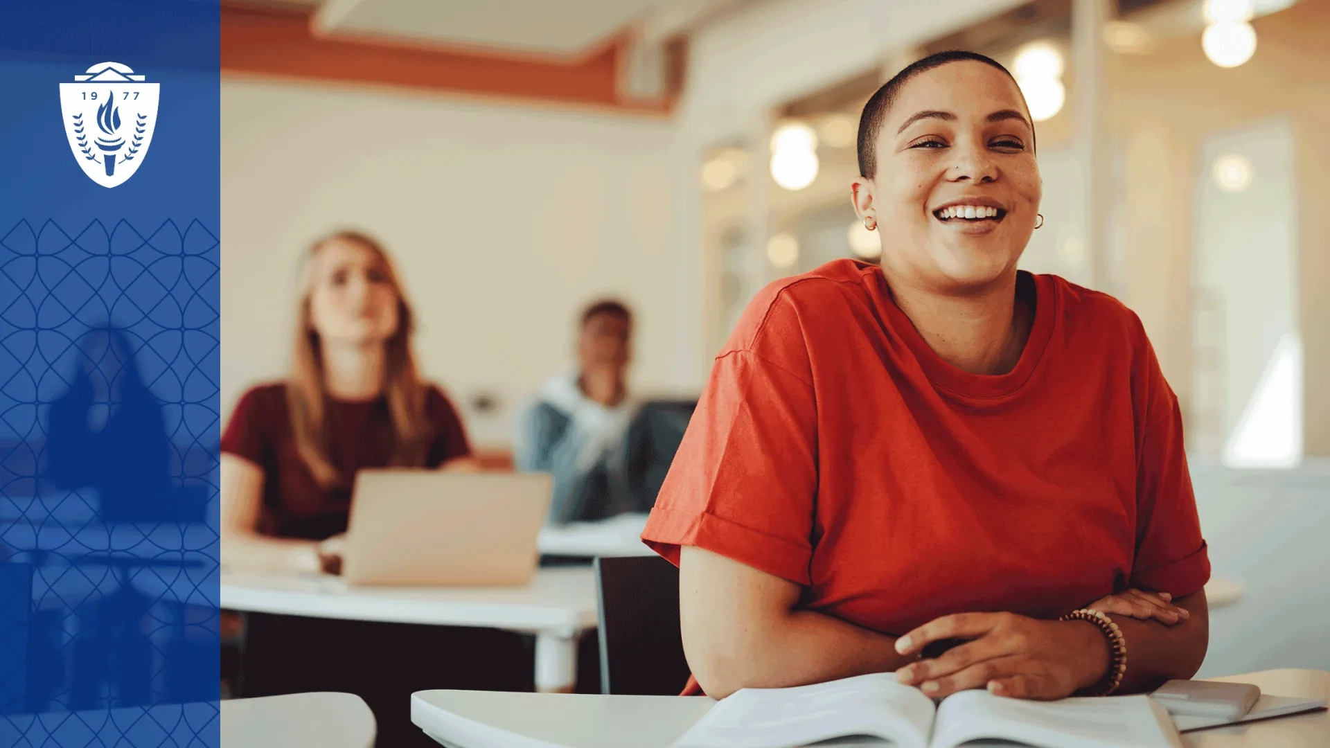 Woman wearing a red shirt sitting a desk in a classroom with a textbook open on the desk