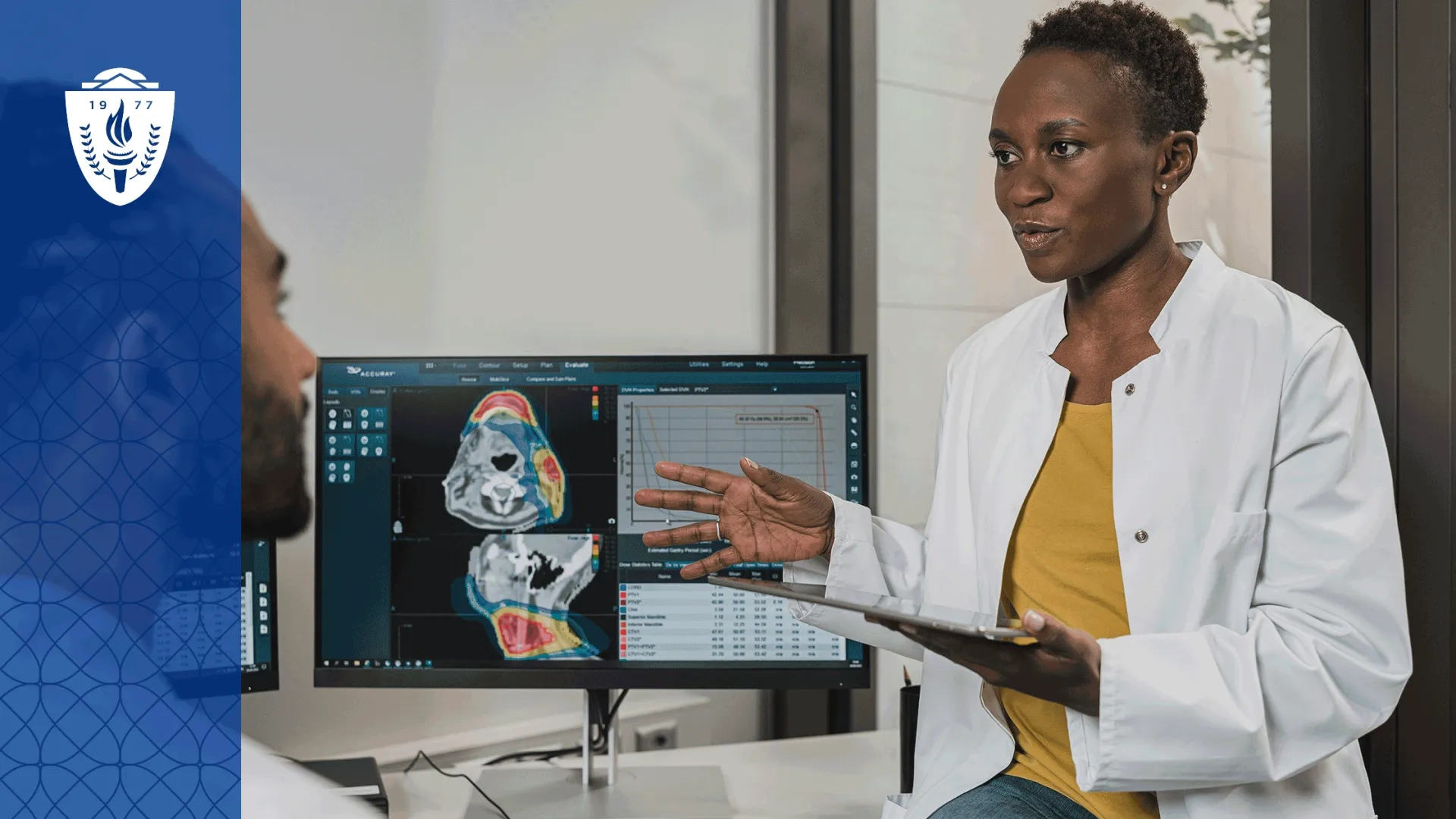Woman wearing white lab coat standing in front of screen showing medical scans