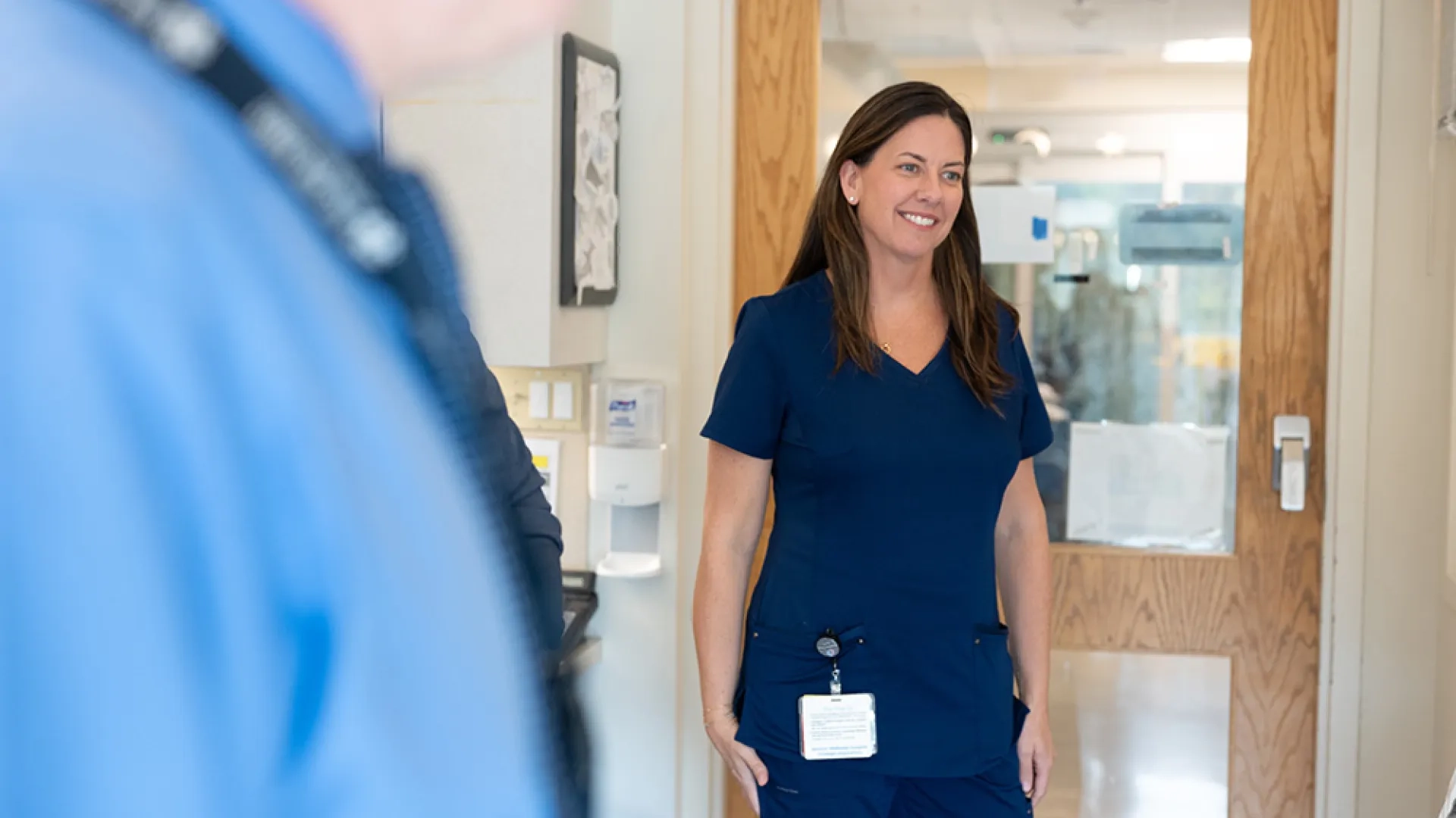A woman wearing medical scrubs stands in a hospital room