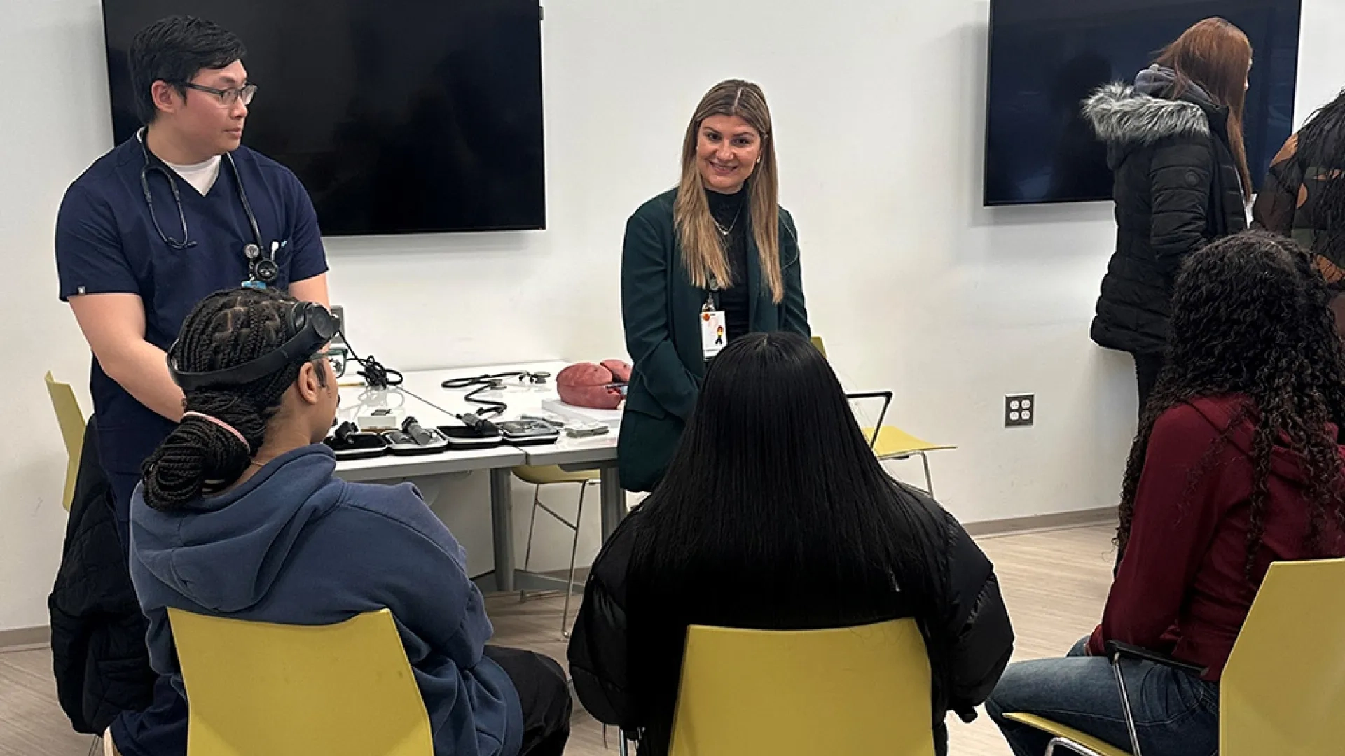 Two people stand in front of three people sitting in chairs