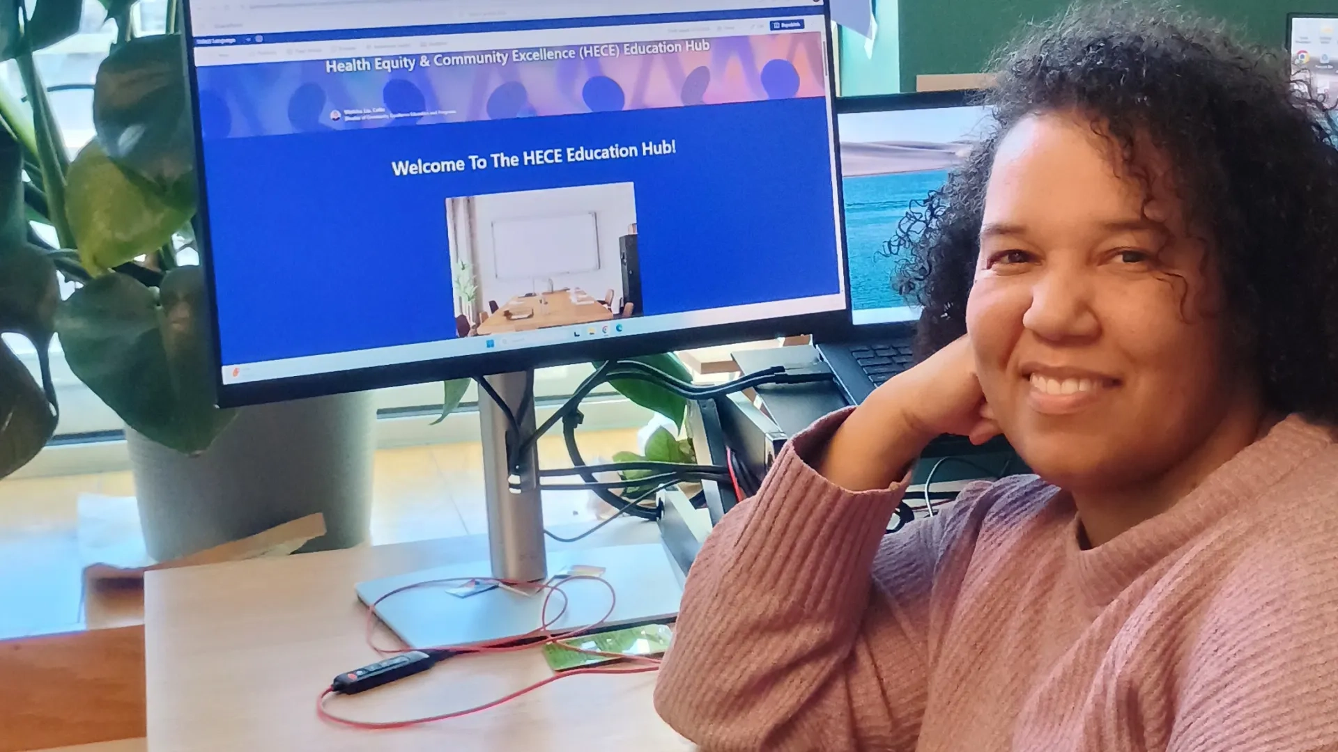 A woman looks at the camera with a computer screen behind her