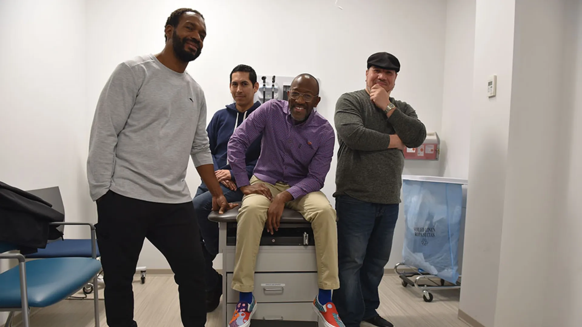 Four men pose in a hospital room 