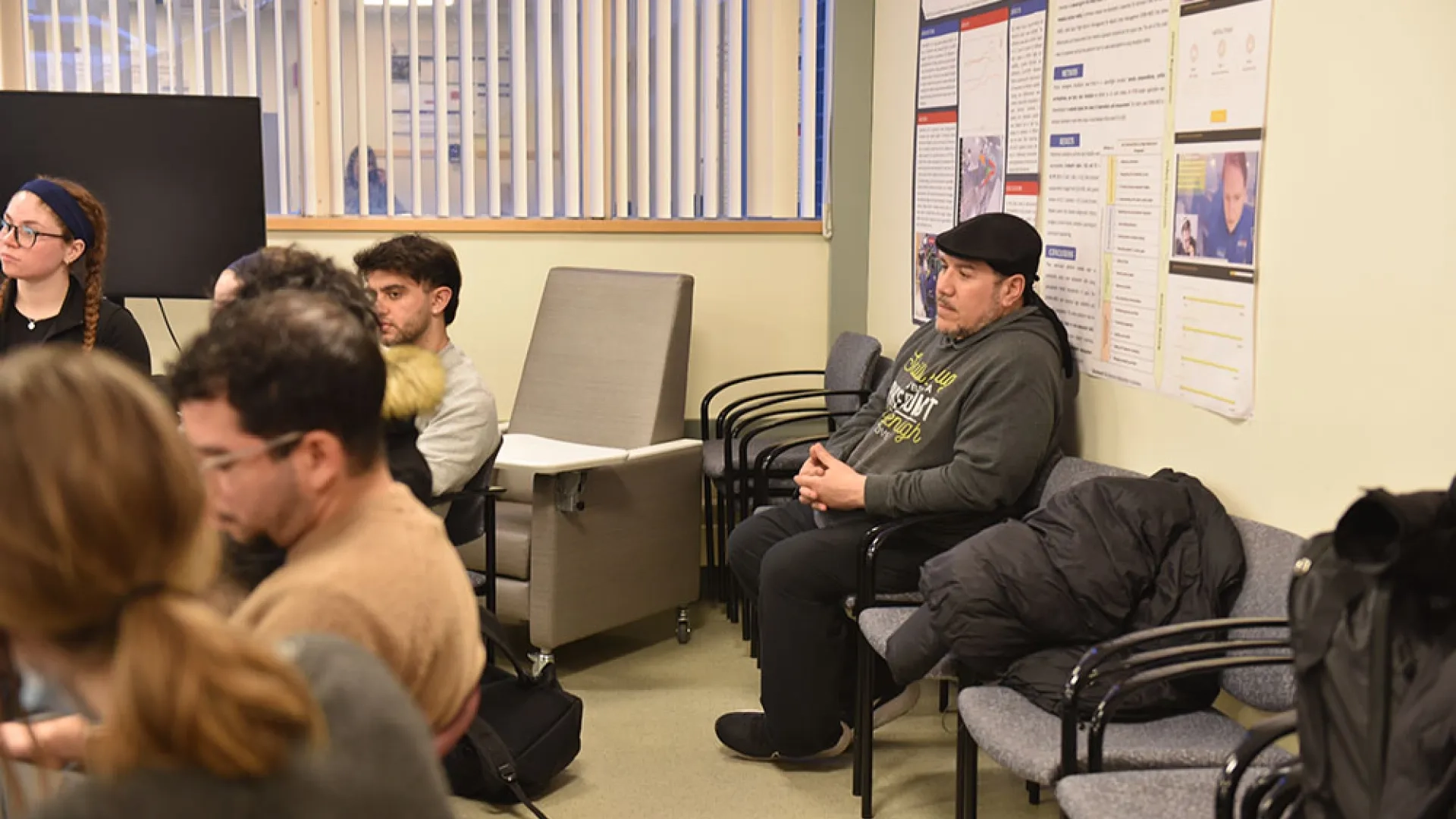 A man sits against a wall while a row of people sit in front of him.