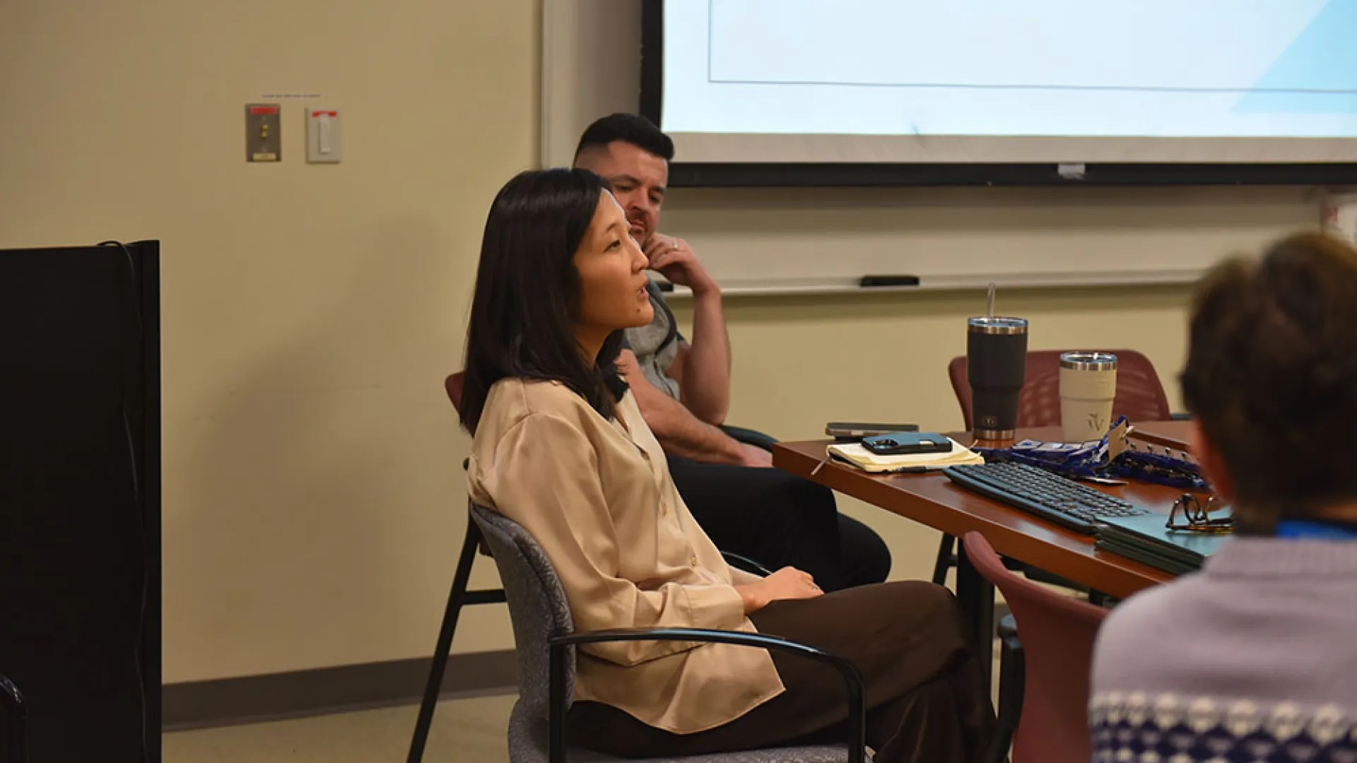A woman sits at a table talking while a man to her left listens
