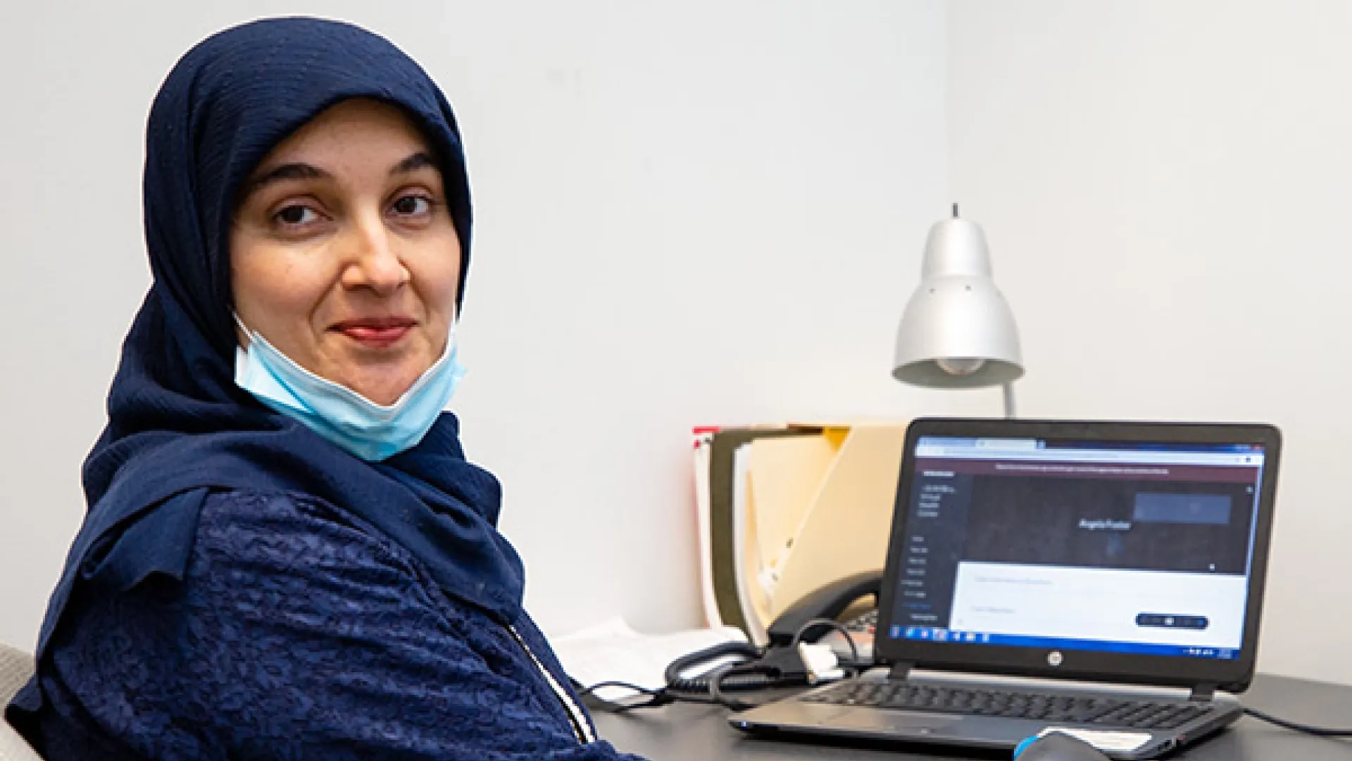 A woman sits at a desk with a laptop computer in front of her