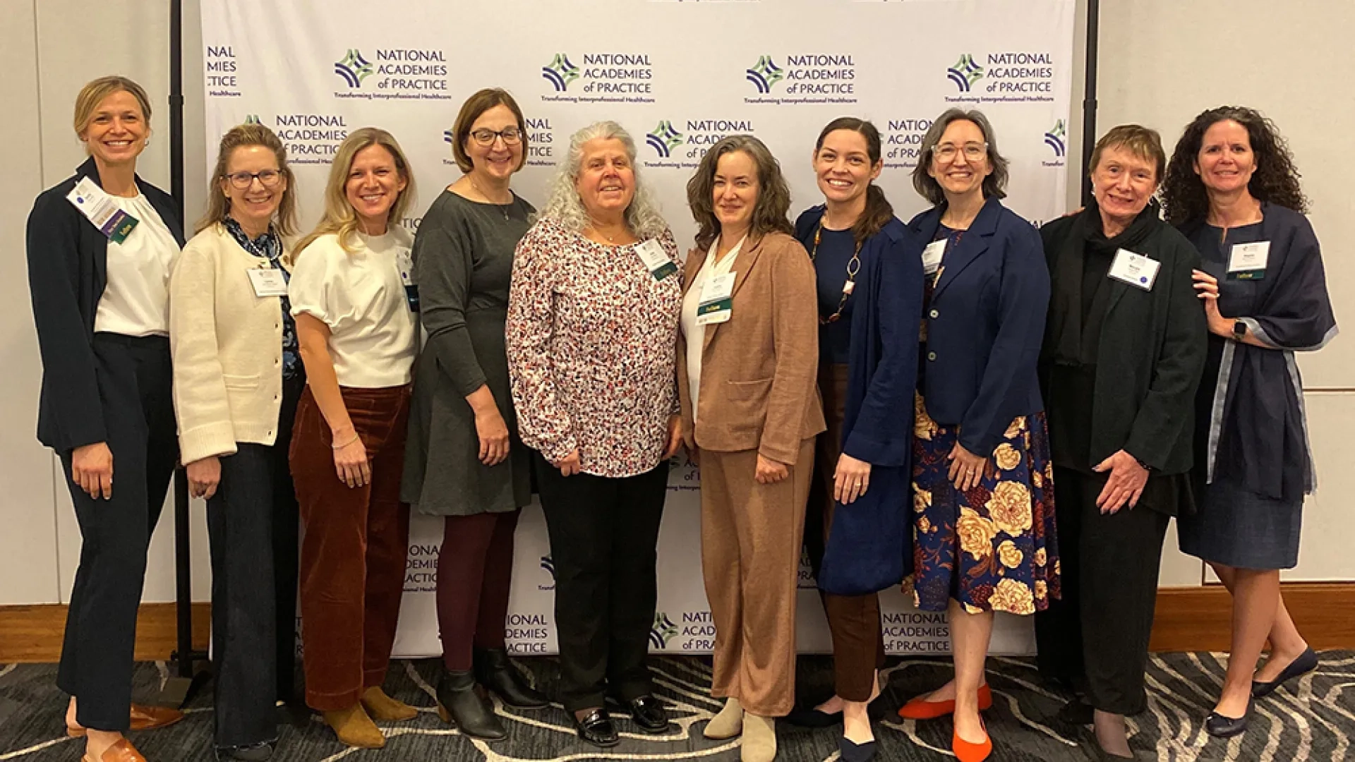 Ten women stand in front of a backdrop posing for a photo