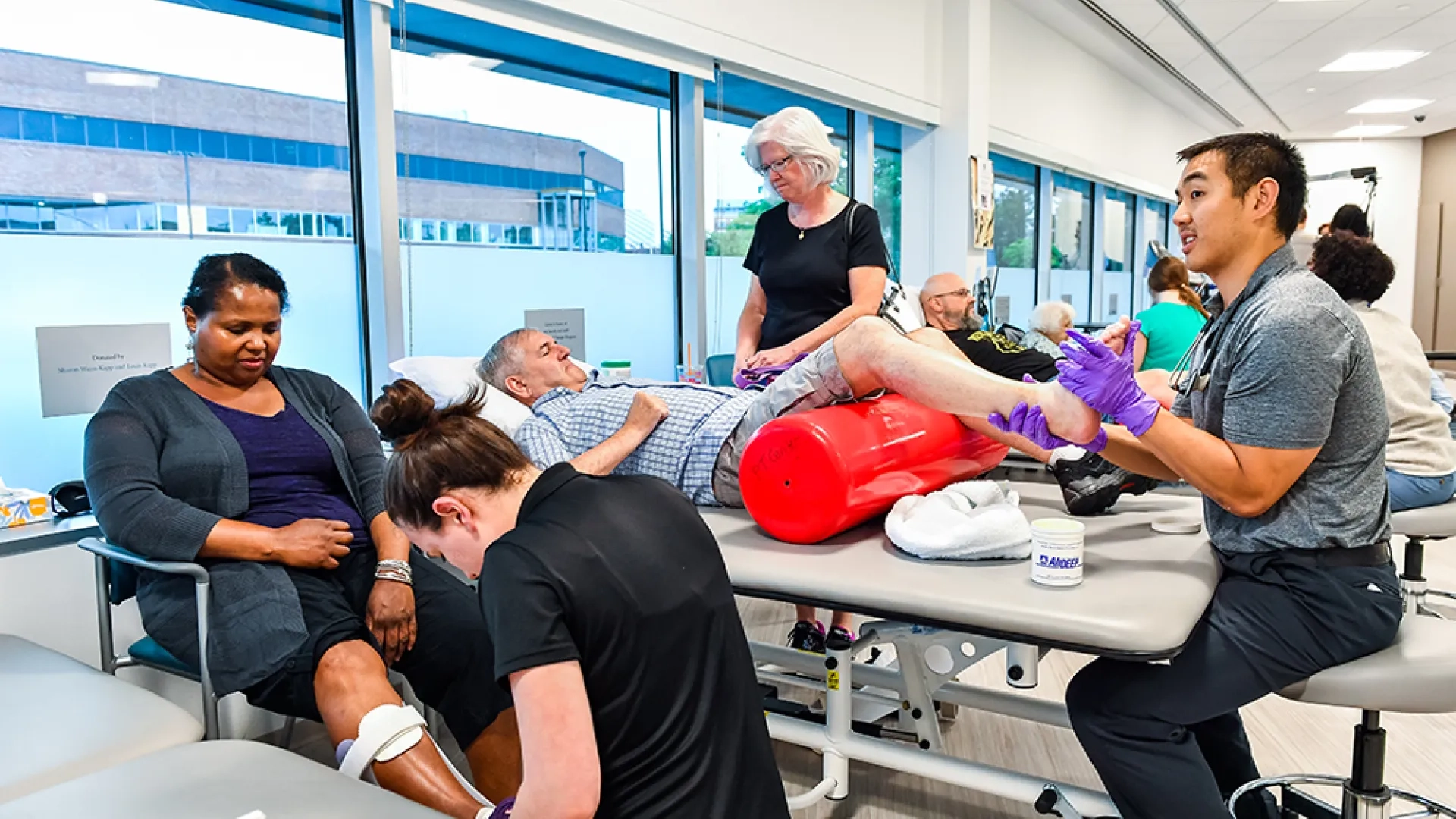 Patients sit on chairs or lie on a table while medical professionals interact with their limbs