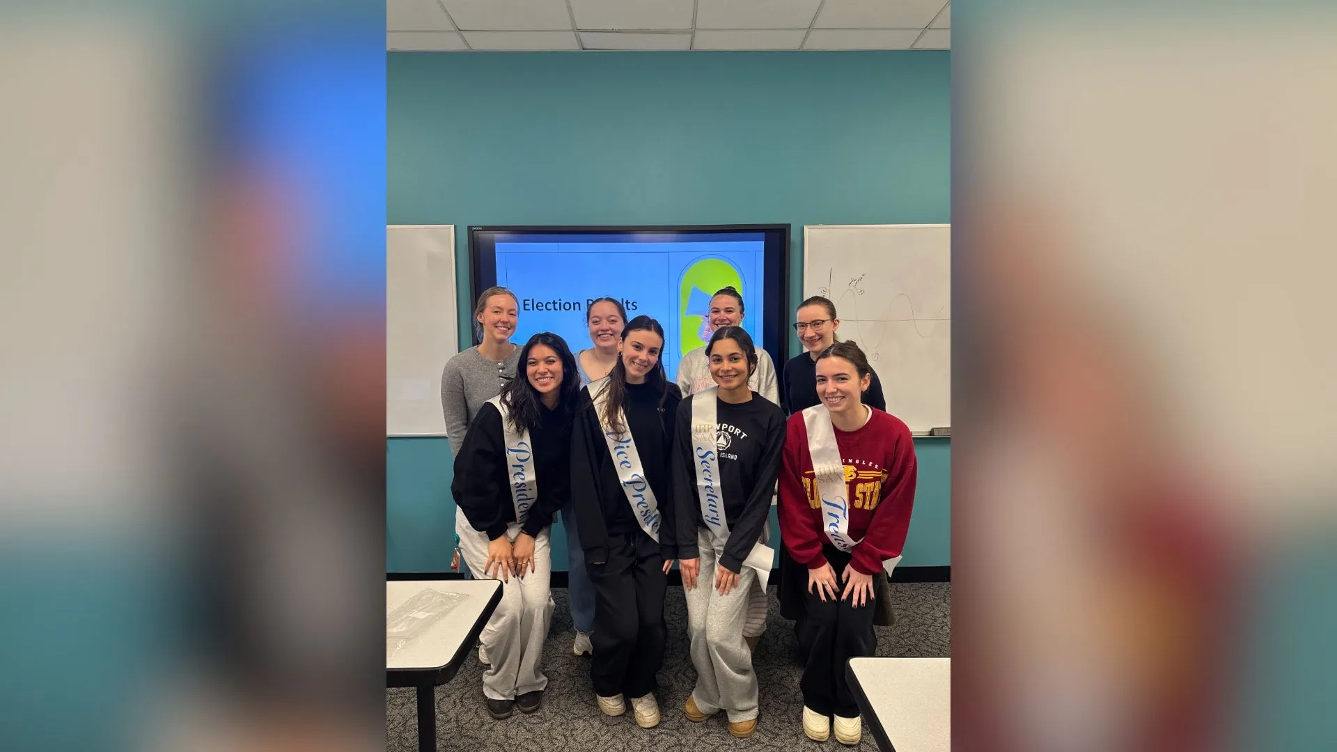 8 women standing in front of a screen with sashes on 