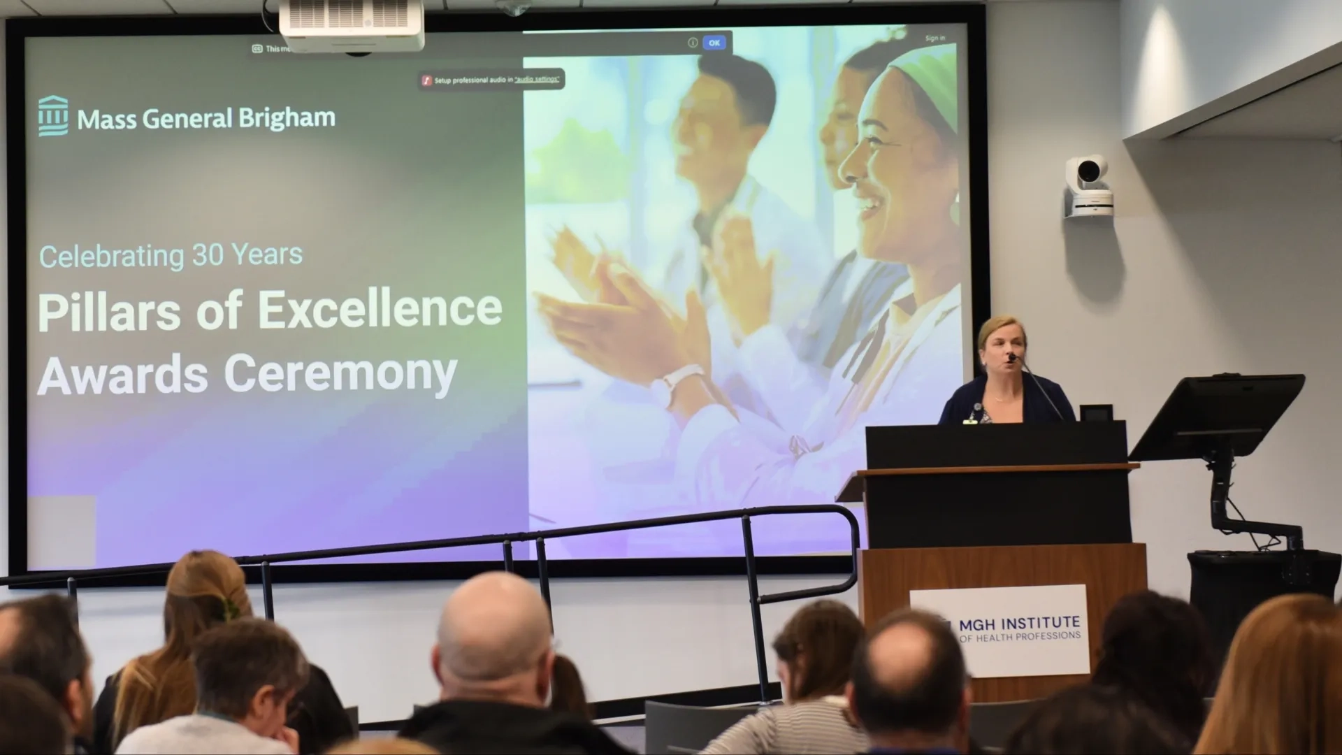 A woman talks at a podium in front of a screen
