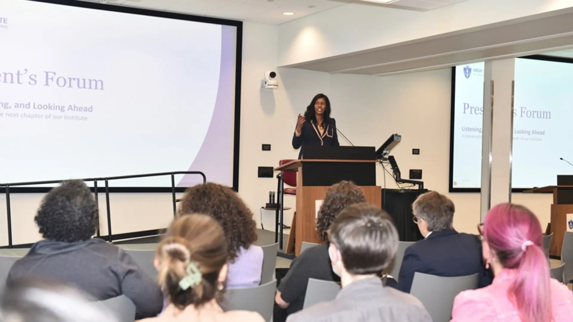 IHP President Deborah Jones speaking at a podium to seated forum attendees