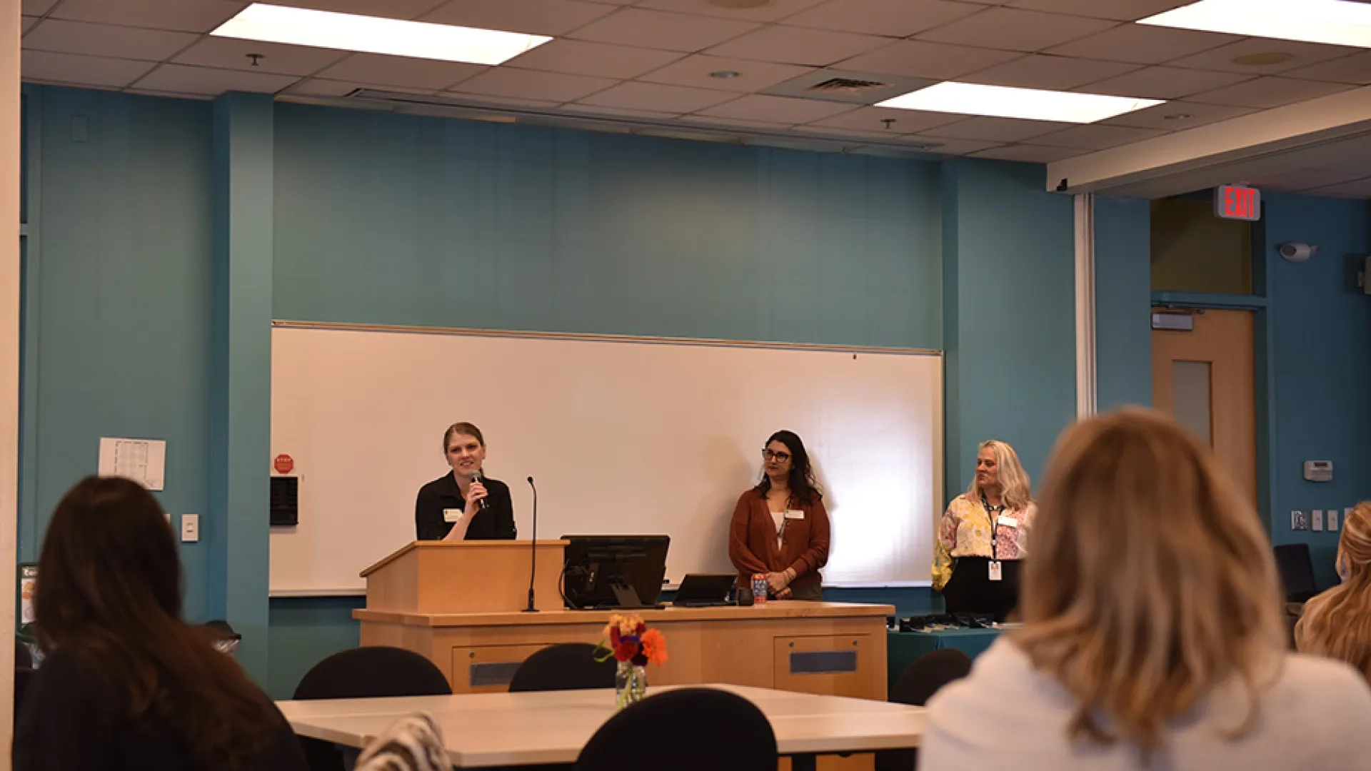 A woman speaks at a podium while two others look on