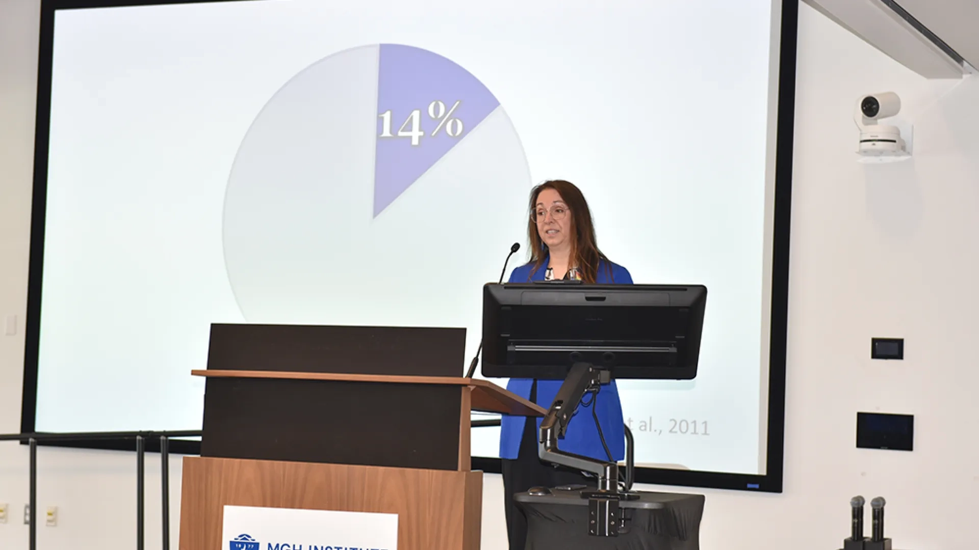 A woman stands at a podium with a screen behind her discussing implementation science