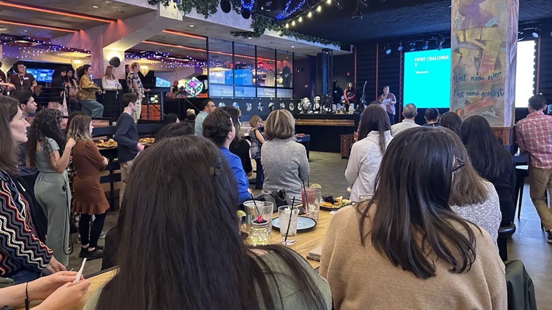 A crowd of people looks to the stage at the front of an employee event