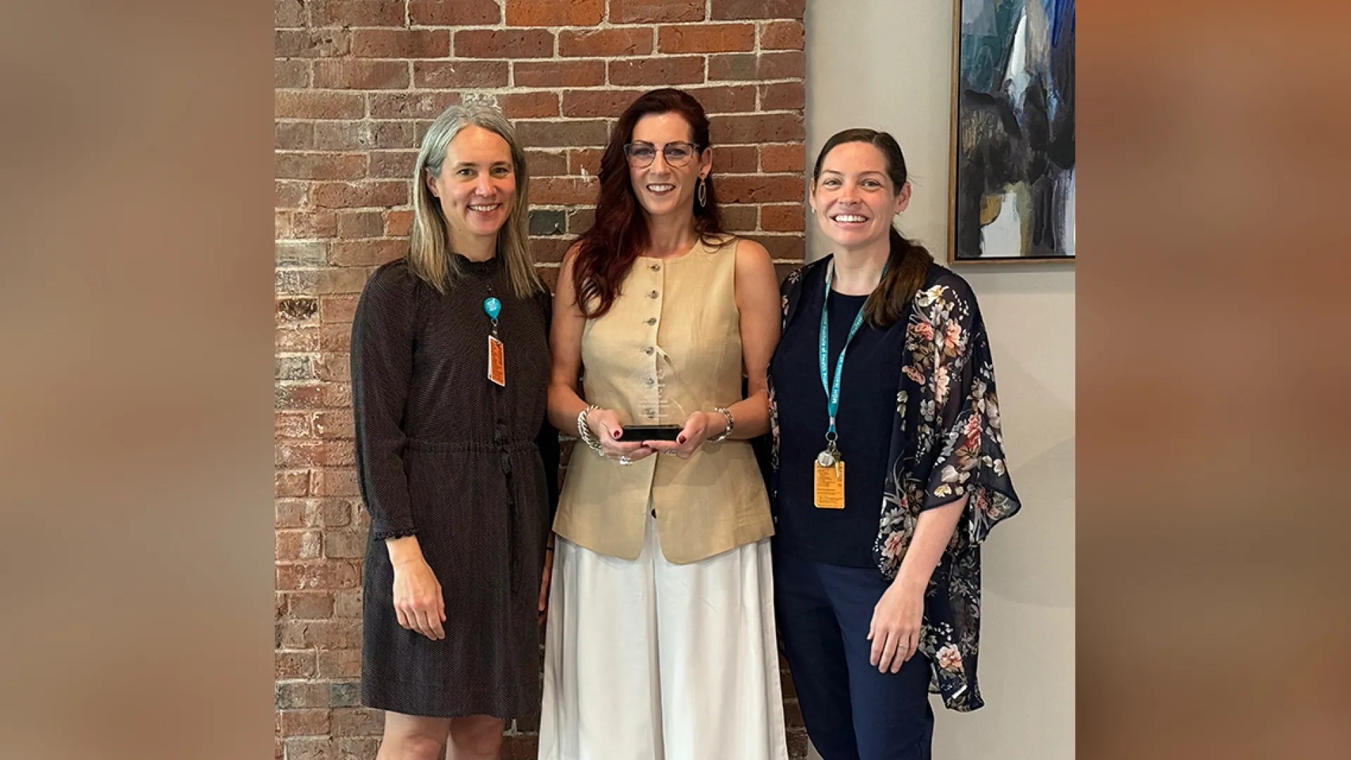 Three women pose with the one in the middle holding the Center of Excellence Faculty Excellence Award 