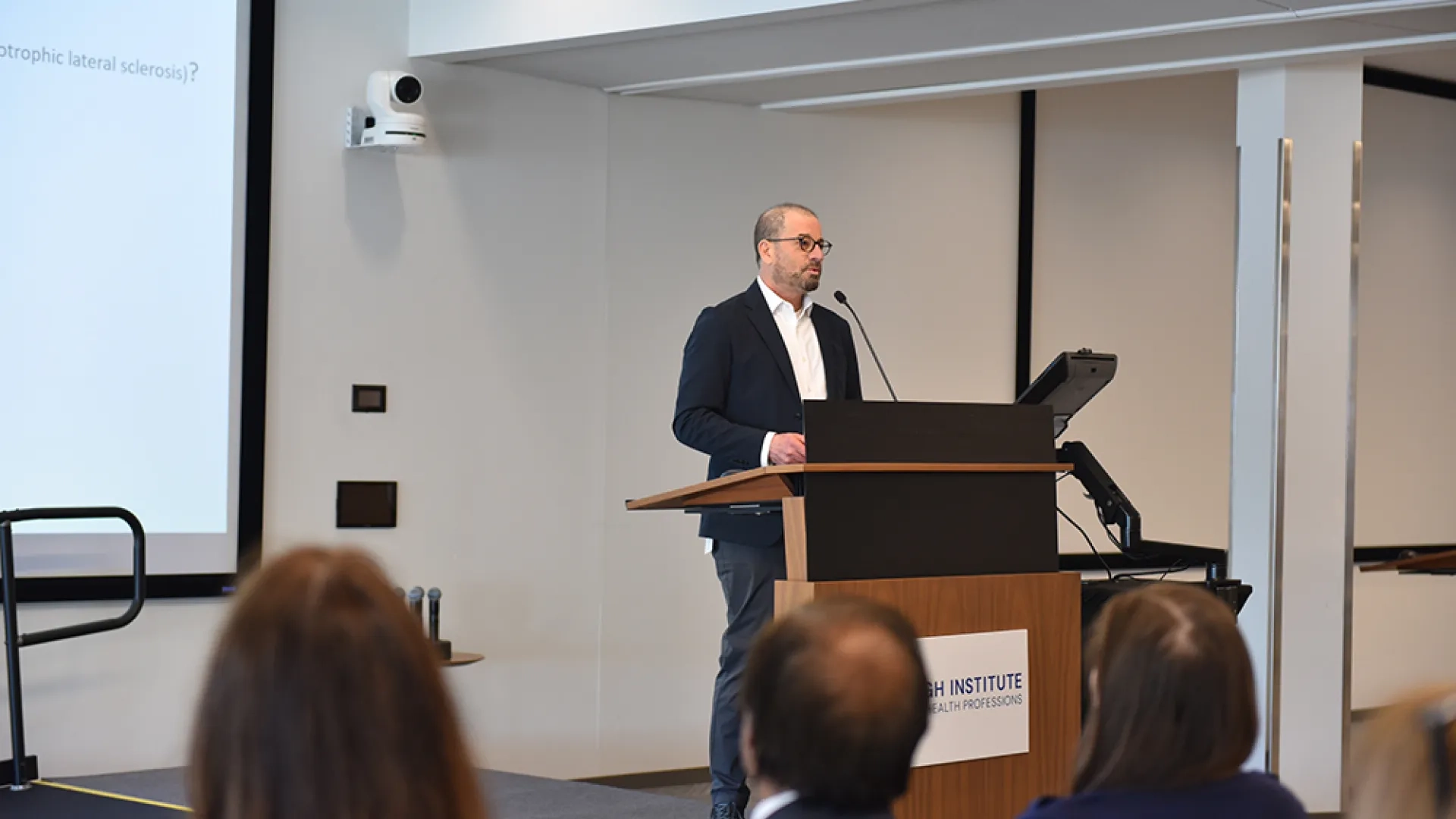 A man stands at a podium discussing clinical applications of speech analytics and AI