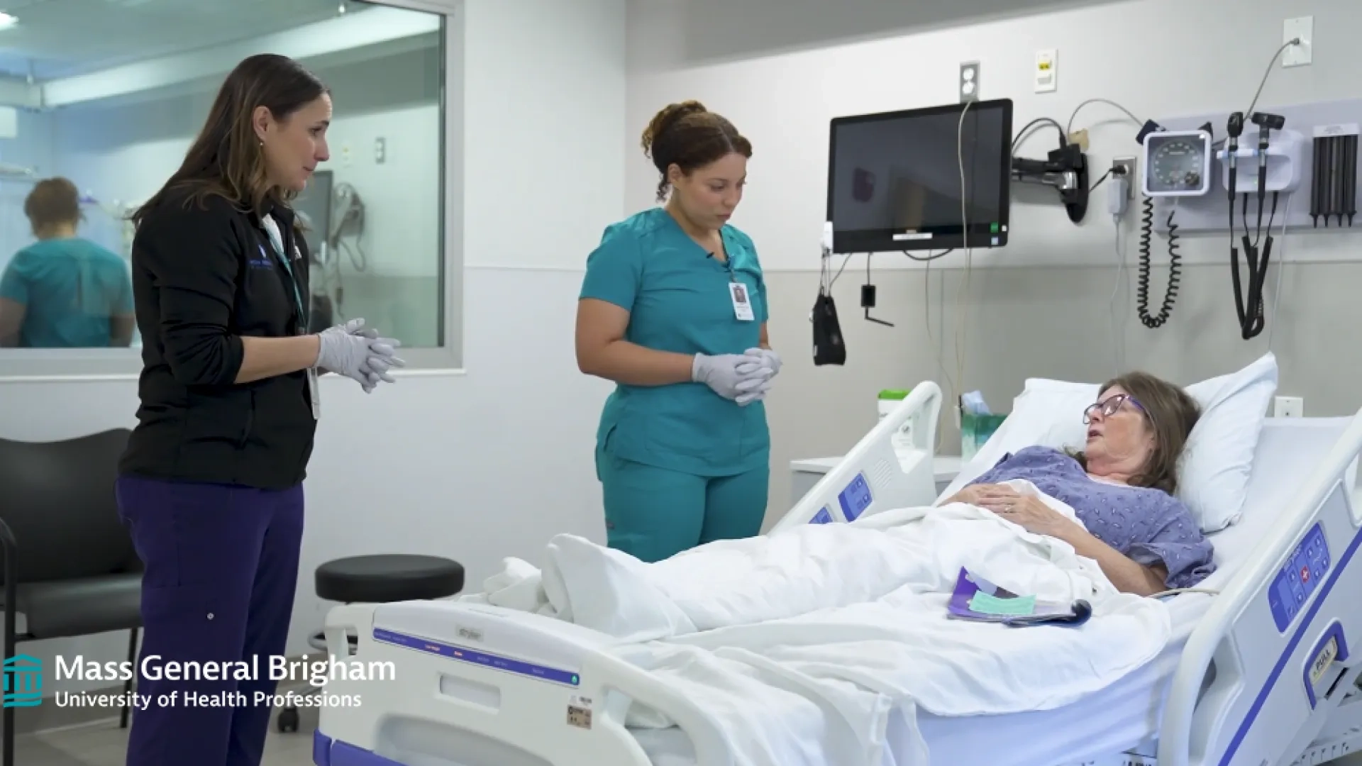 two women in scrubs stand next to an older woman laying in a hospital bed