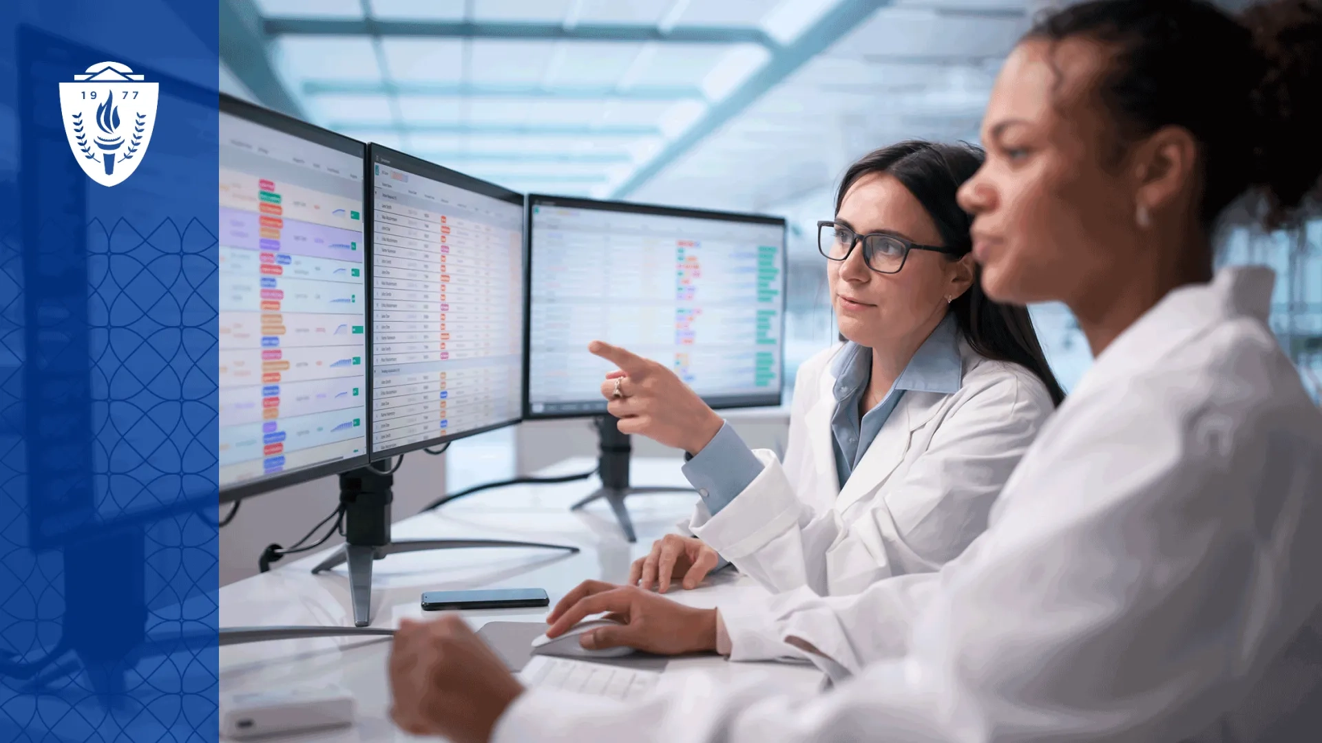 A healthcare educator stands with a small group of nursing and medical learners in a simulation lab reviewing learner analytics on a large display screen. The setting feels collaborative and academic, with realistic clinical equipment and human interaction rather than futuristic technology imagery. 
