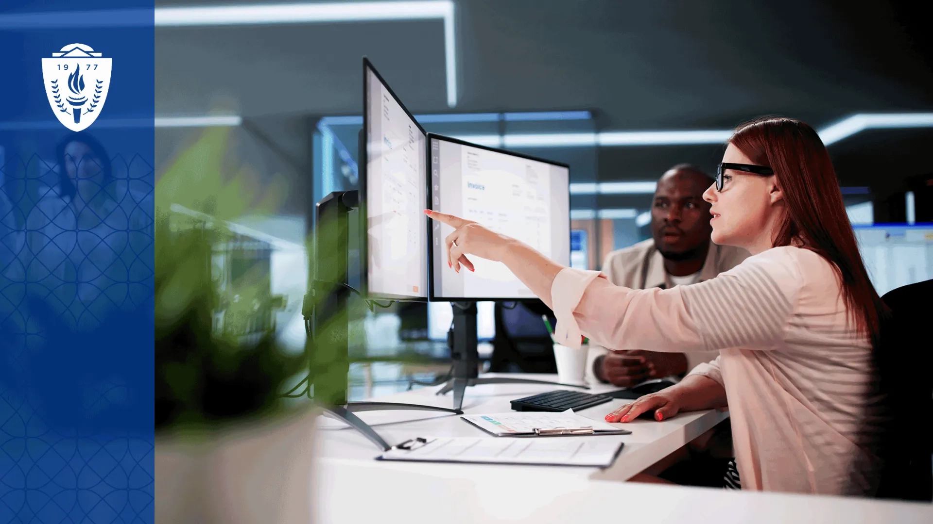 A faculty member reviews several educational technology platforms on dual computer monitors while collaborating with another educator in a modern academic office or simulation center.  