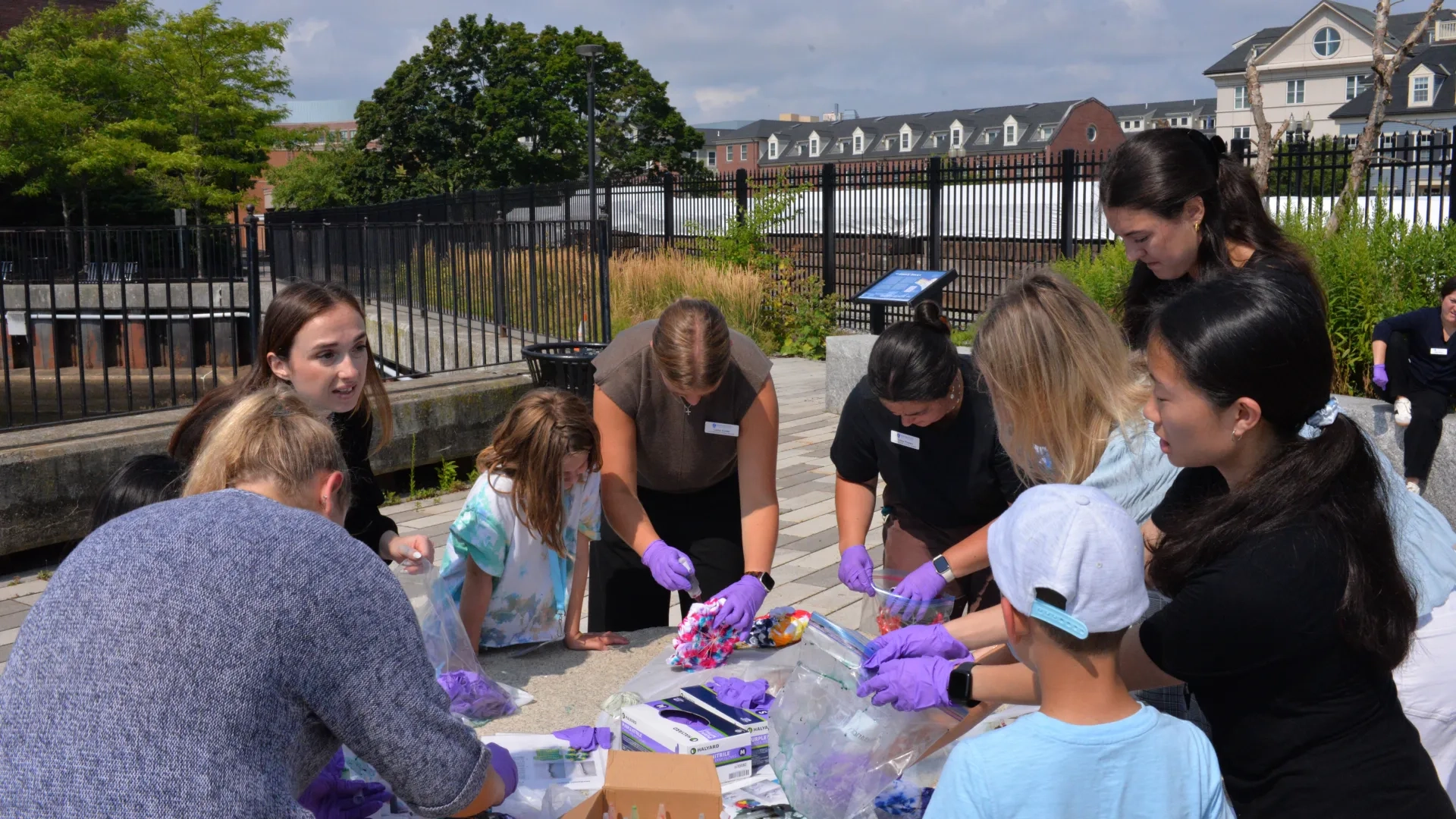 Kids and adult wear purple gloves and stand around a table dying shirts
