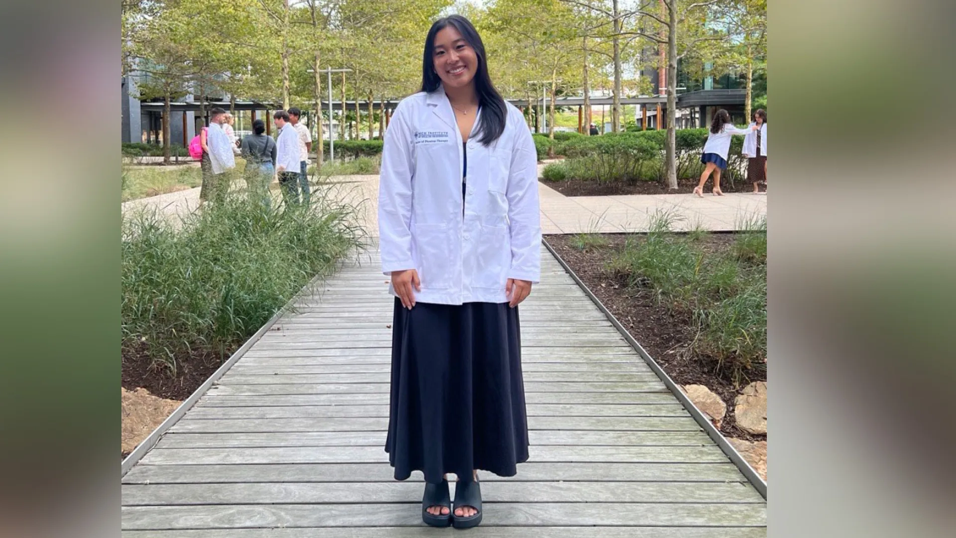 Ashley Ma stands on a walkway with landscaping on the side and trees in the background