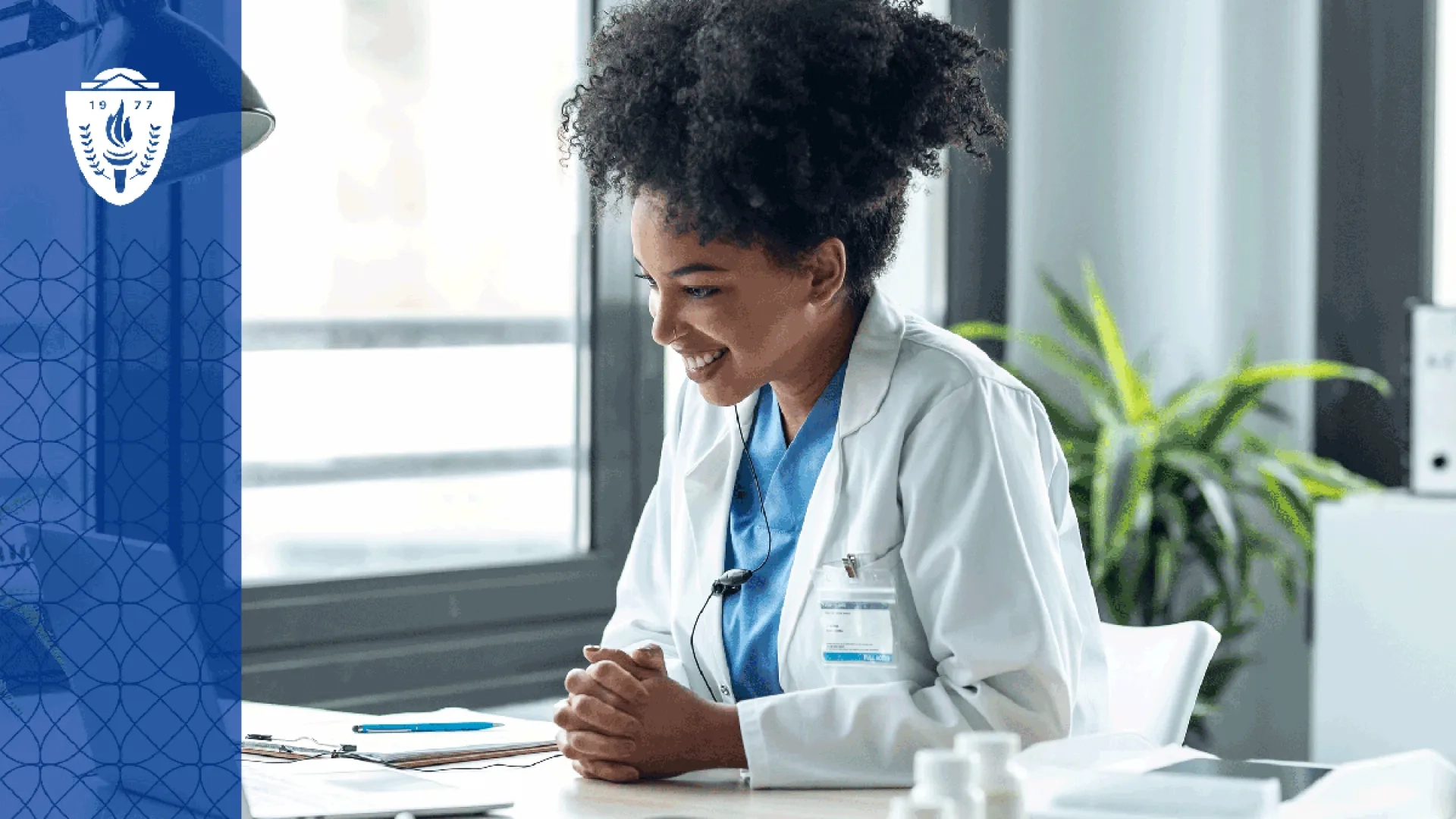 Nurse with frizzy hair wearing a lab coat sitting at a desk looking at a laptop