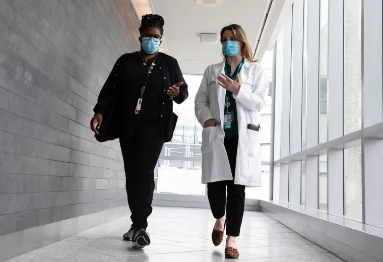 Two people walking down a hallway wearing masks