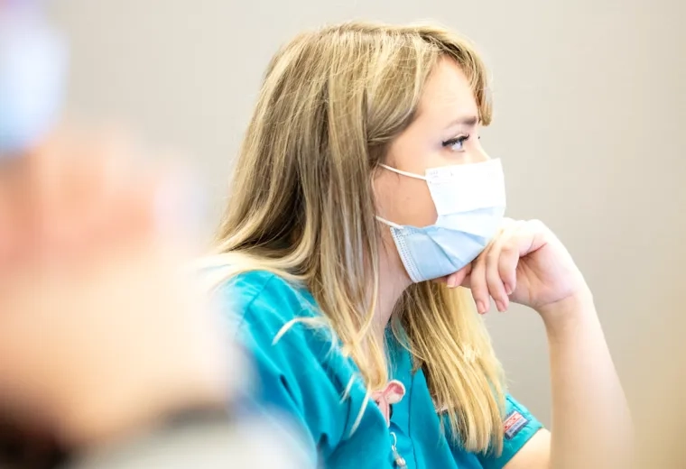 A woman sitting with a mask on and her chin resting on her hand
