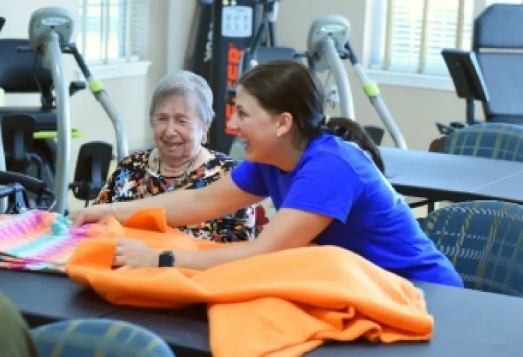 Two women laugh while working on a blanket