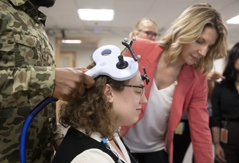 man holds device that looks like a big T to a woman's head while others look at a computer