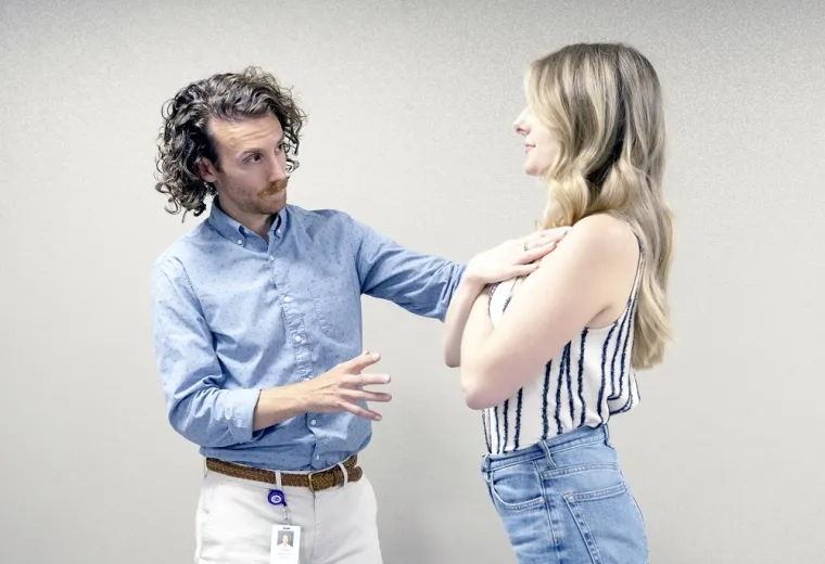 man helps woman who has her arms crossed to stand straight